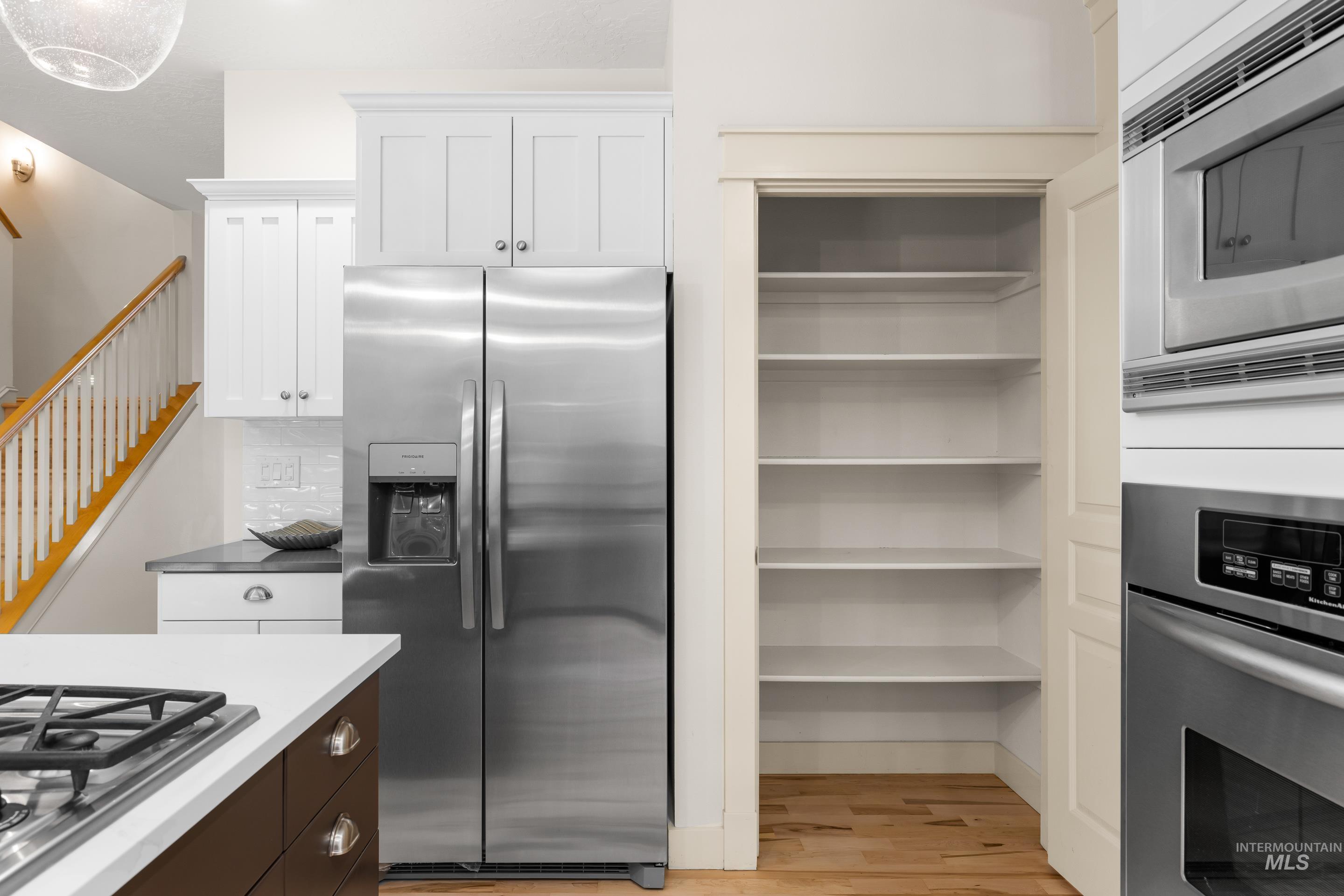 Kitchen with appliances with stainless steel finishes, light wood finished floors, dark brown cabinets, and white cabinetry