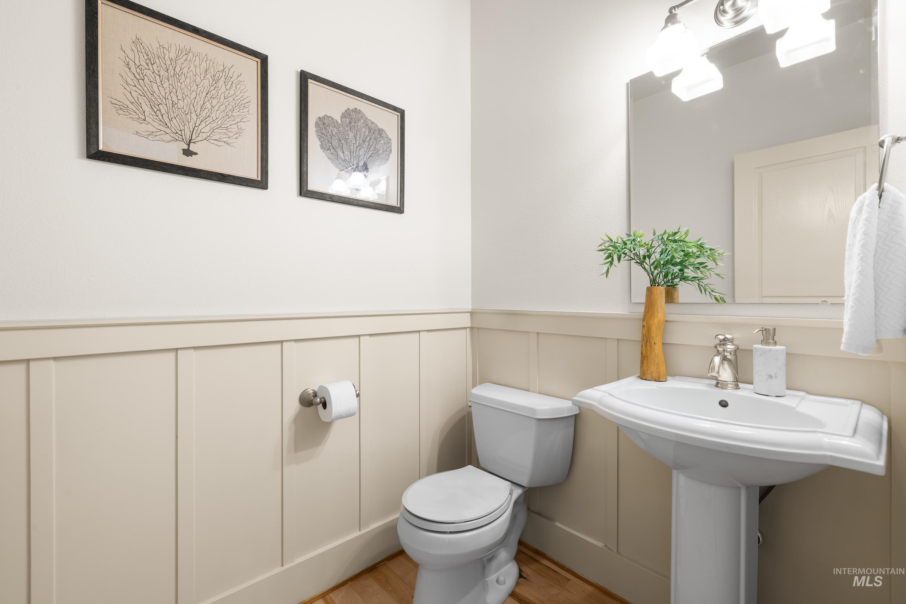 Half bathroom with a wainscoted wall, light wood finished floors, and a decorative wall