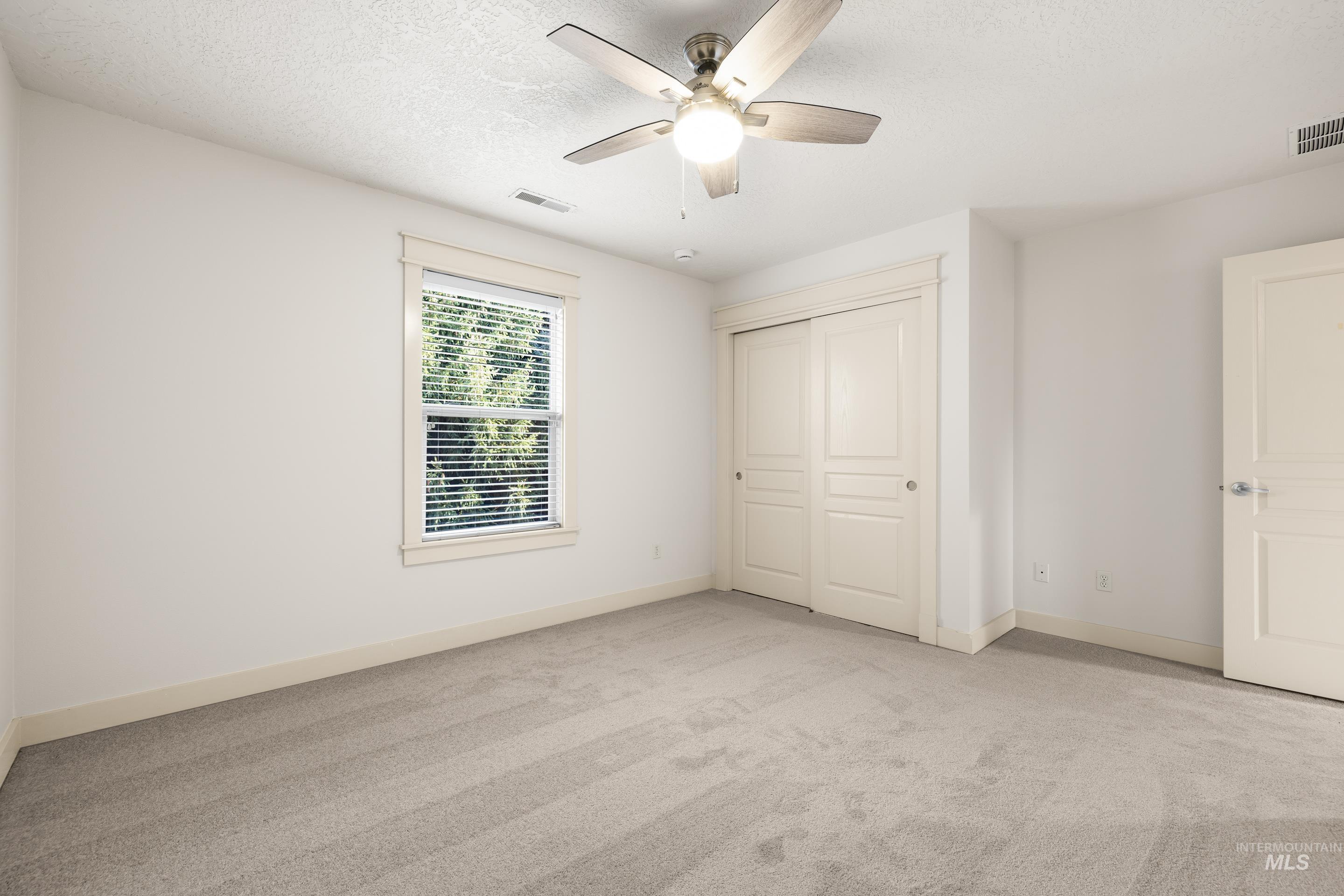 Unfurnished bedroom with light colored carpet, ceiling fan, a textured ceiling, and a closet