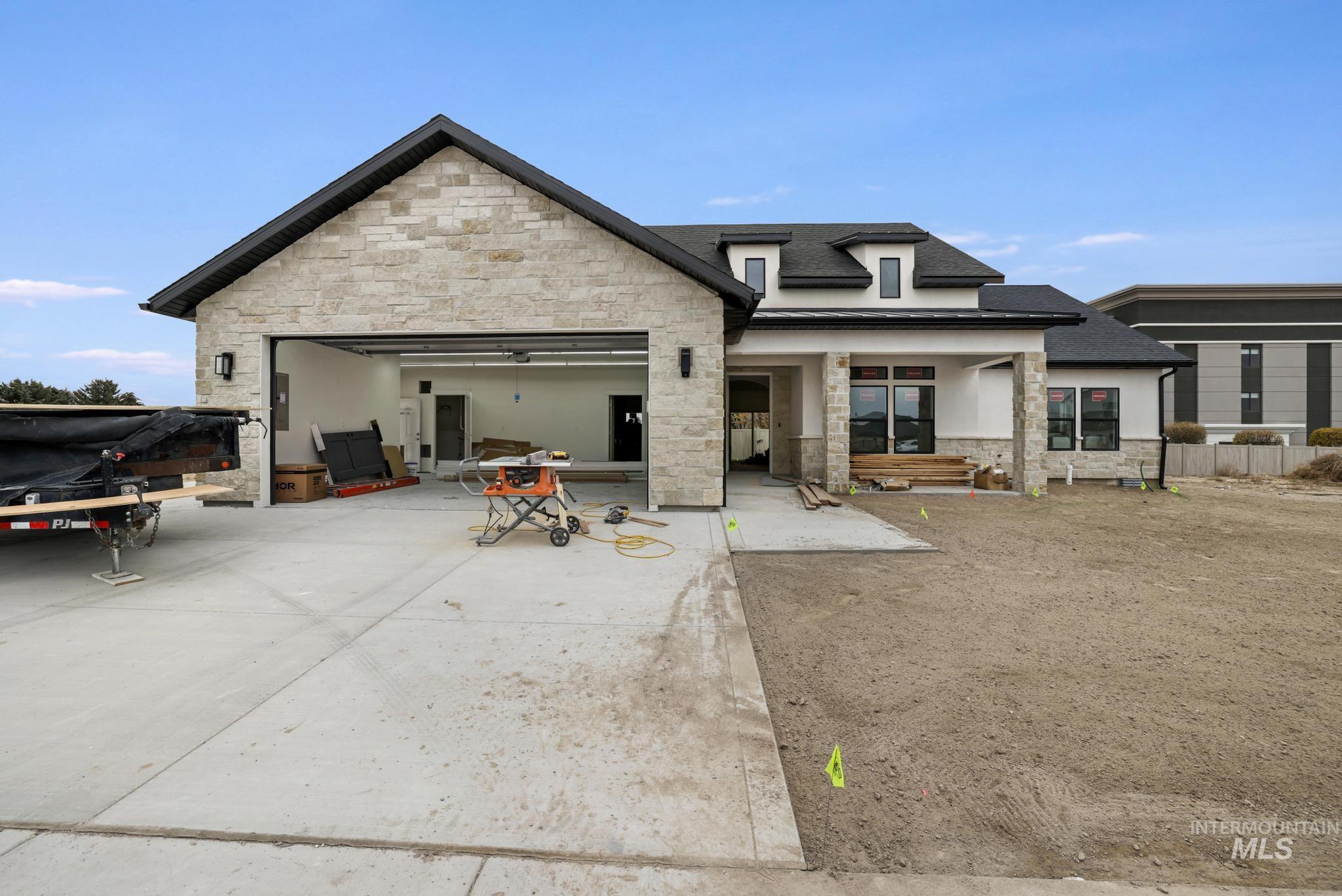 Back of property with stone siding, a patio area, concrete driveway, an attached garage, and roof with shingles