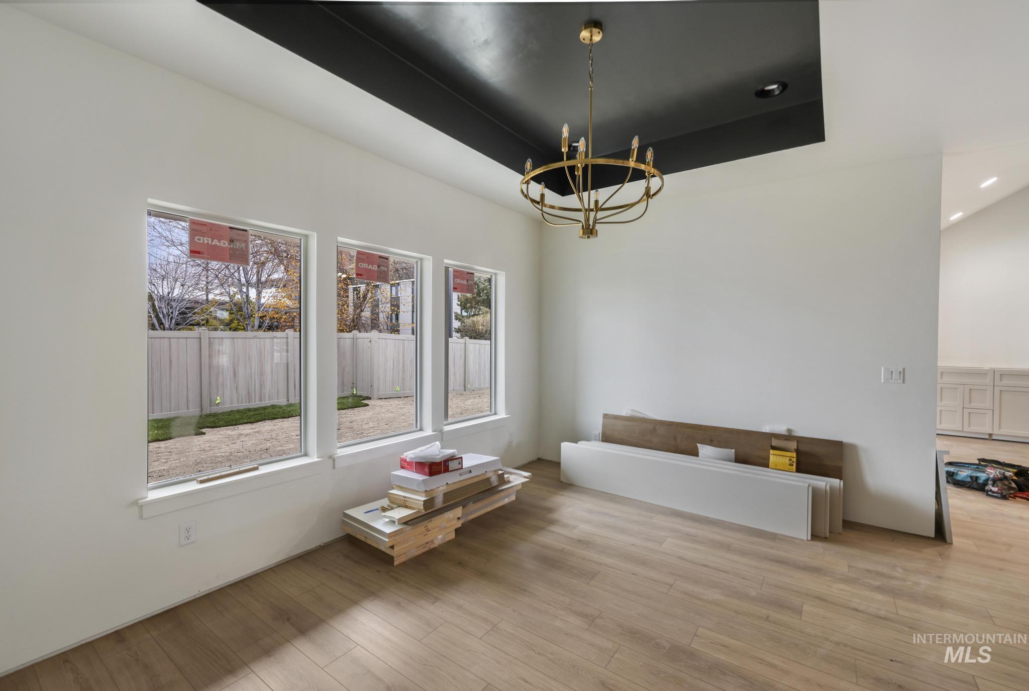 Unfurnished dining area with a tray ceiling, a chandelier, and wood finished floors