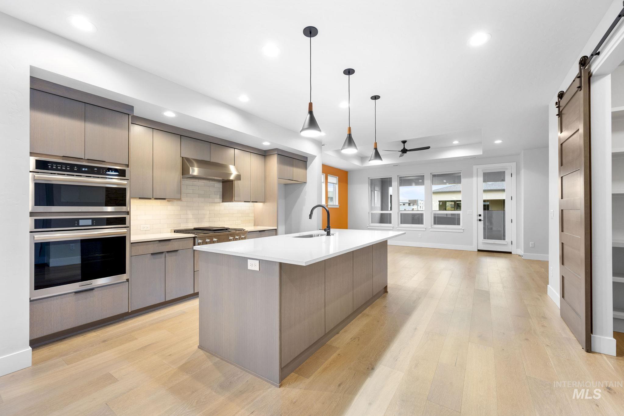 Kitchen with a barn door, modern cabinets, backsplash, pendant lighting, and gray cabinetry