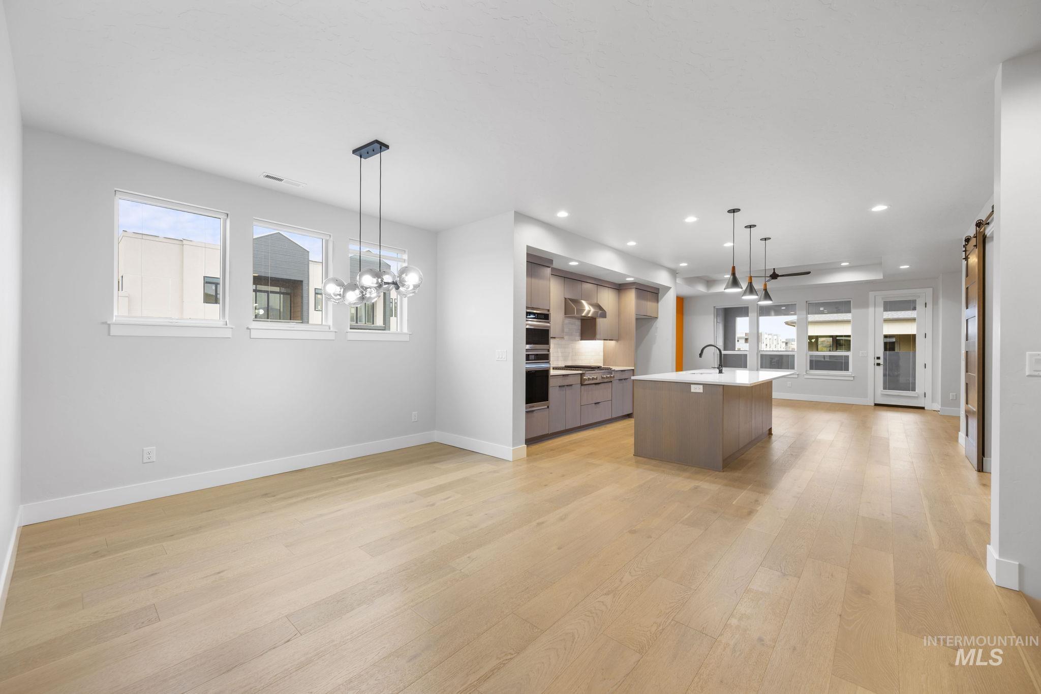 Kitchen featuring modern cabinets, open floor plan, a kitchen island with sink, hanging light fixtures, and light wood-type flooring