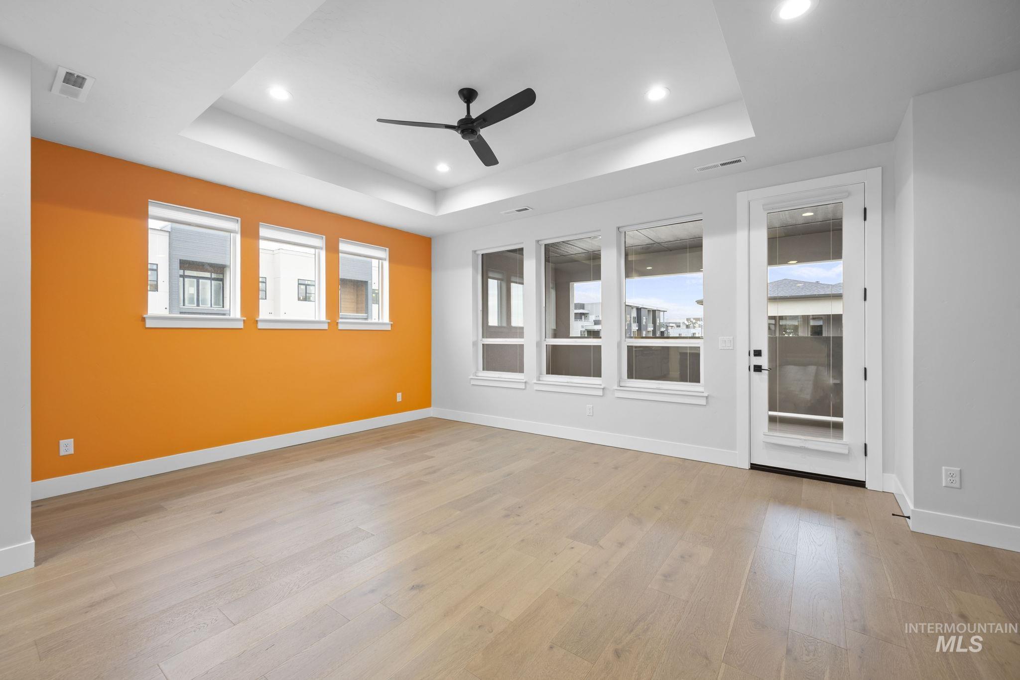 Empty room featuring a tray ceiling, ceiling fan, light wood-style flooring, and recessed lighting
