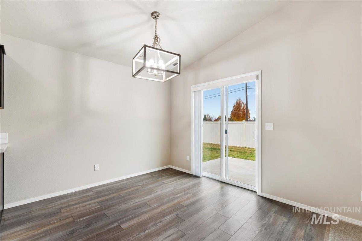 Unfurnished dining area with dark wood finished floors, vaulted ceiling, and a chandelier