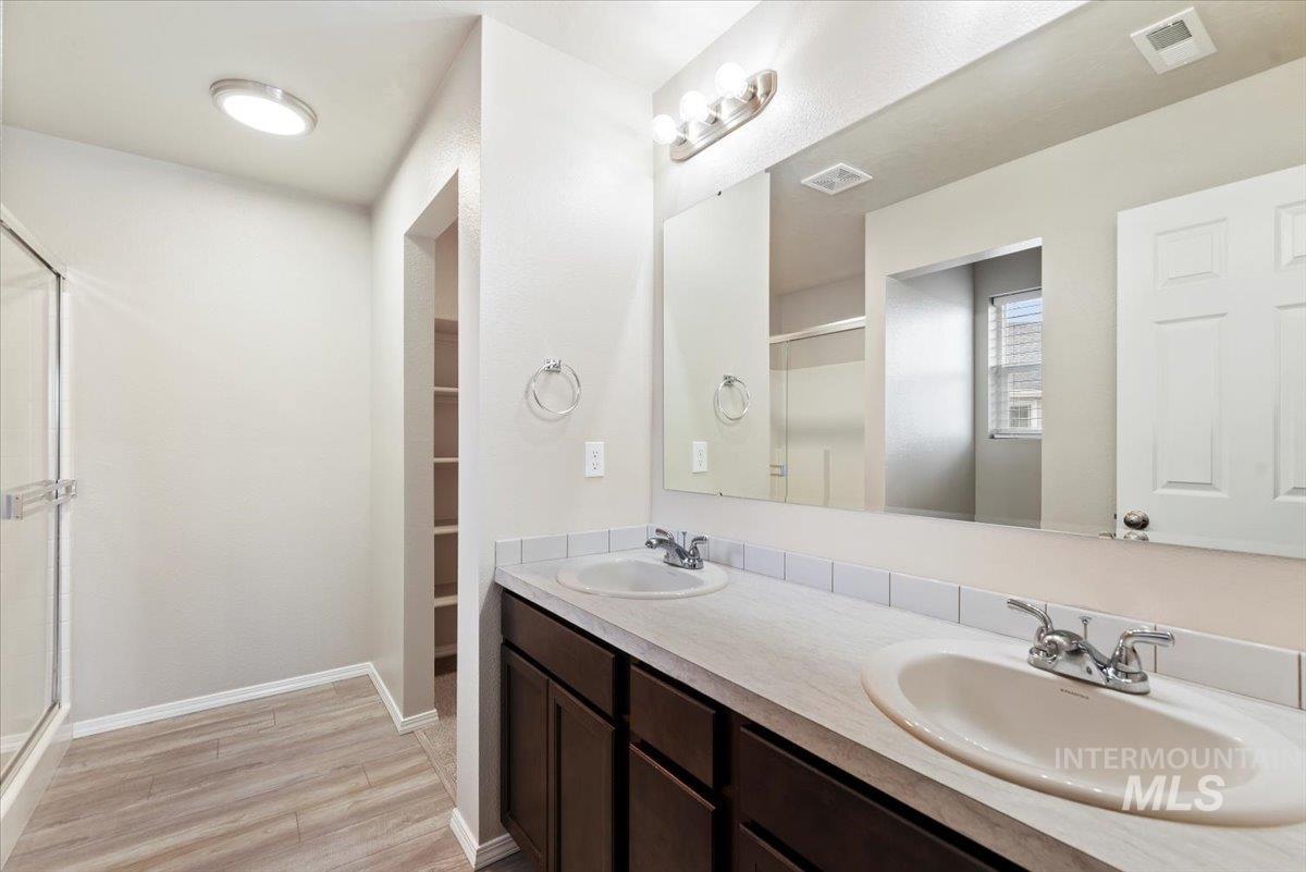 Bathroom with double vanity, light wood-style flooring, a shower stall, and a spacious closet