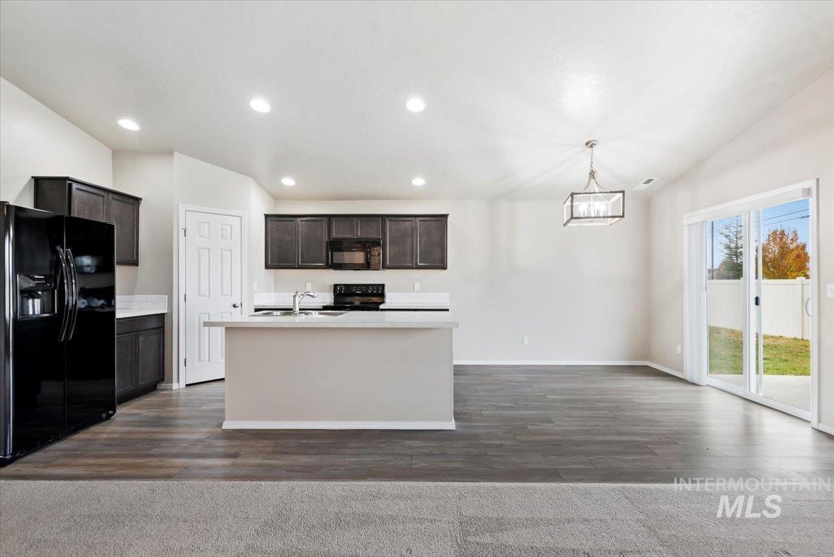 Kitchen featuring black appliances, dark brown cabinets, recessed lighting, dark wood-style flooring, and a kitchen island with sink