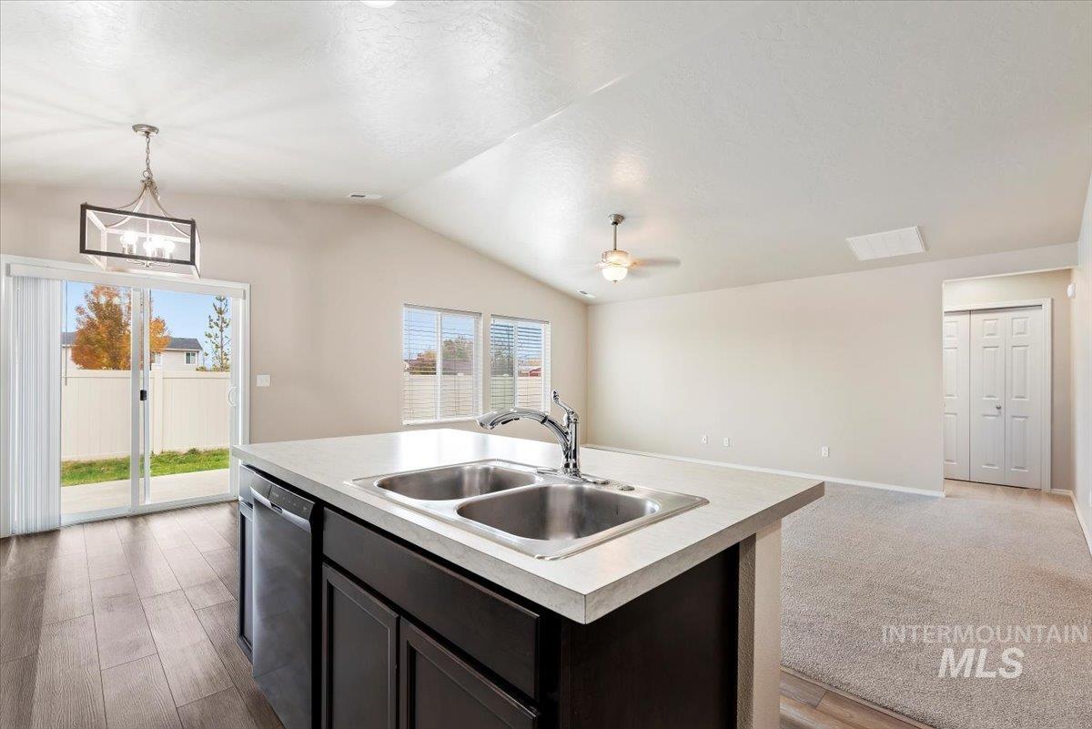 Kitchen featuring open floor plan, light countertops, lofted ceiling, a center island with sink, and dishwasher