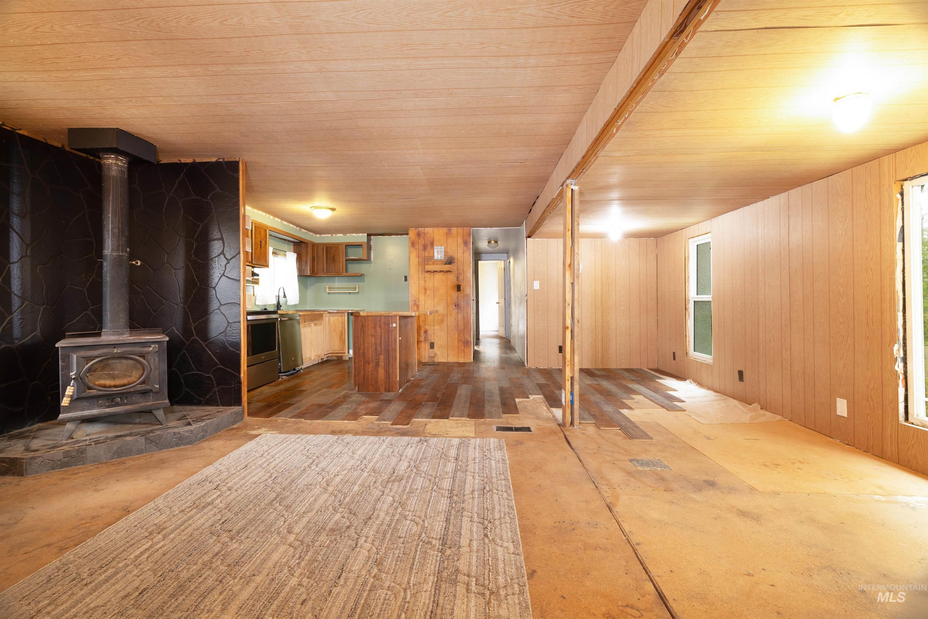 Unfurnished living room with a wood stove, wood ceiling, and wooden walls