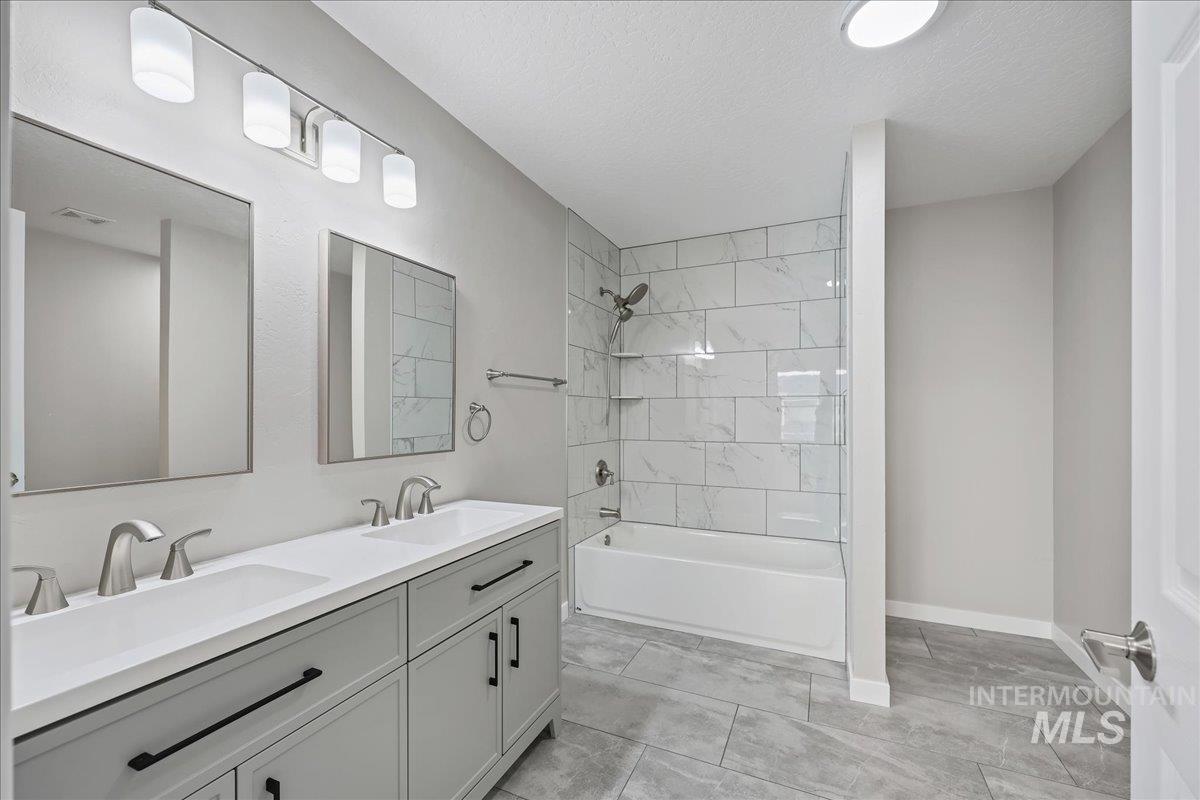 Bathroom featuring a textured ceiling, double vanity, and bathtub / shower combination