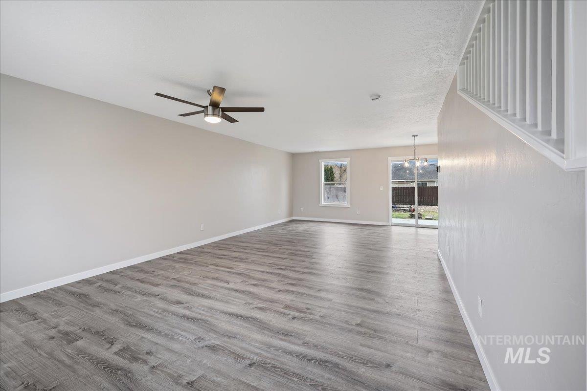 Unfurnished living room featuring light wood finished floors, a chandelier, a ceiling fan, and a textured ceiling