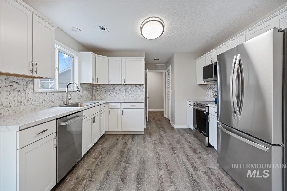 Kitchen with stainless steel appliances, backsplash, light countertops, light wood-type flooring, and a textured ceiling
