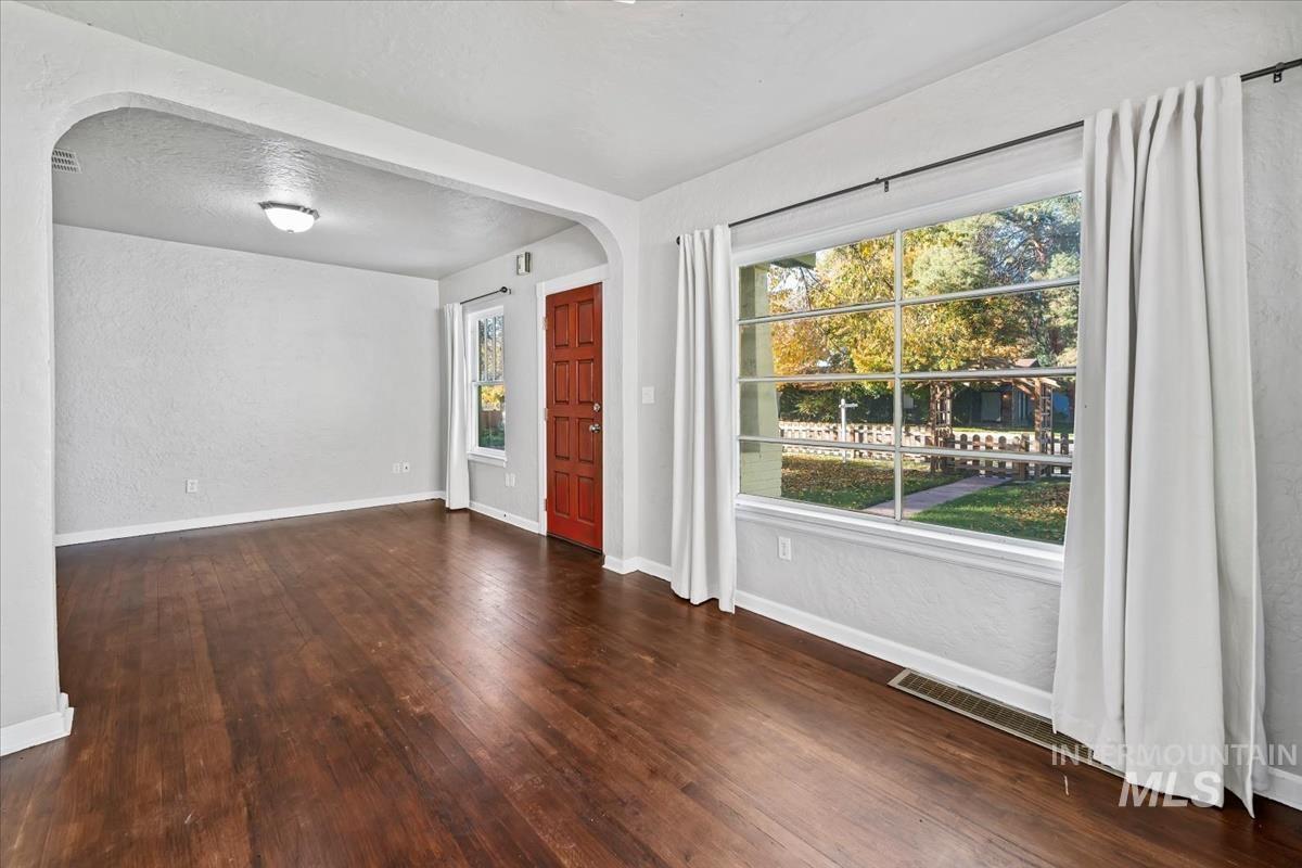 Spare room featuring a textured wall, arched walkways, dark wood-type flooring, and a textured ceiling