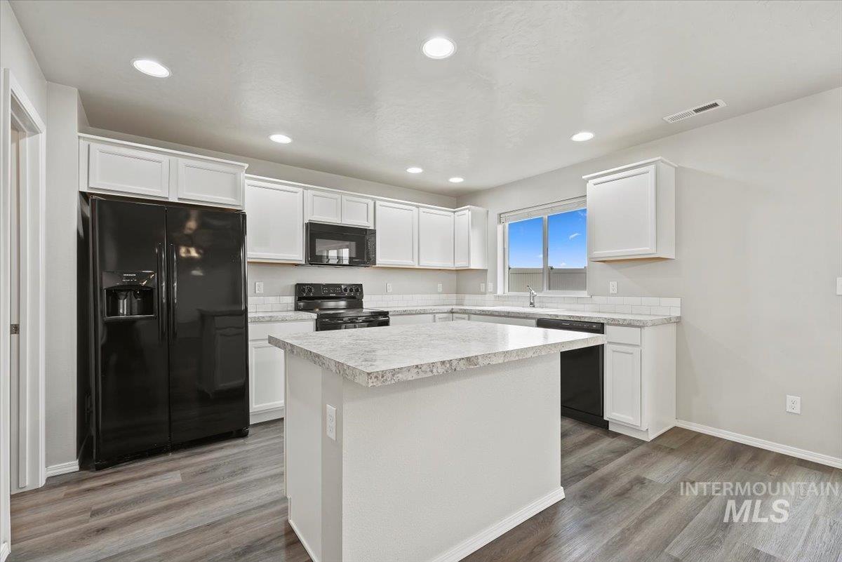 Kitchen with black appliances, light countertops, white cabinets, and recessed lighting