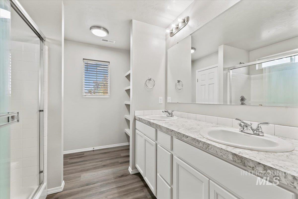 Bathroom featuring double vanity, a stall shower, and dark wood-style floors