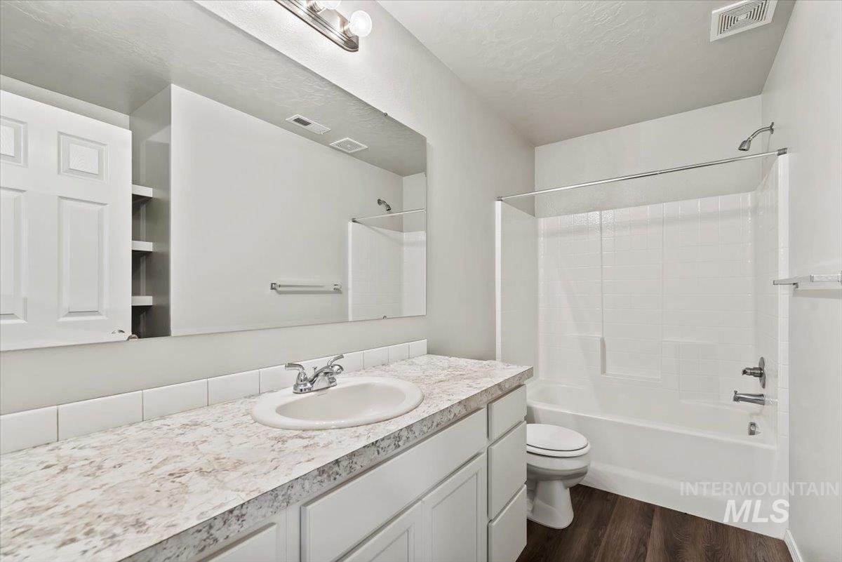 Full bathroom featuring dark wood-style floors, vanity, shower / tub combination, and a textured ceiling