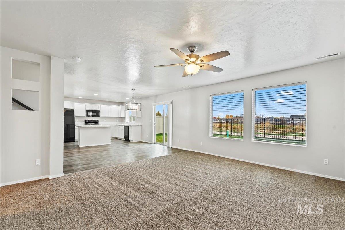 Unfurnished living room featuring a textured ceiling, ceiling fan, plenty of natural light, and dark colored carpet