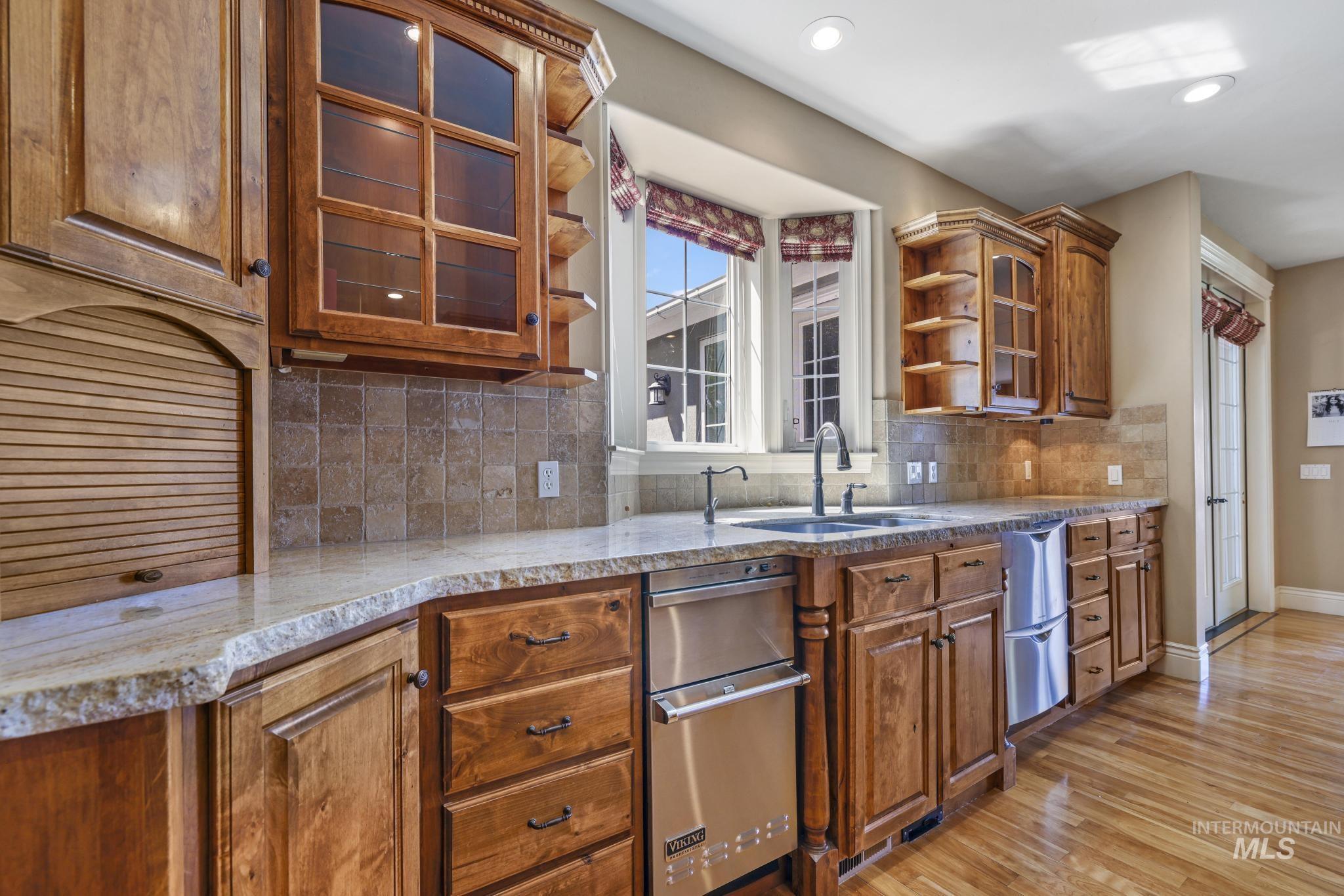 Kitchen featuring glass insert cabinets, brown cabinetry, tasteful backsplash, light wood-style floors, and light stone countertops
