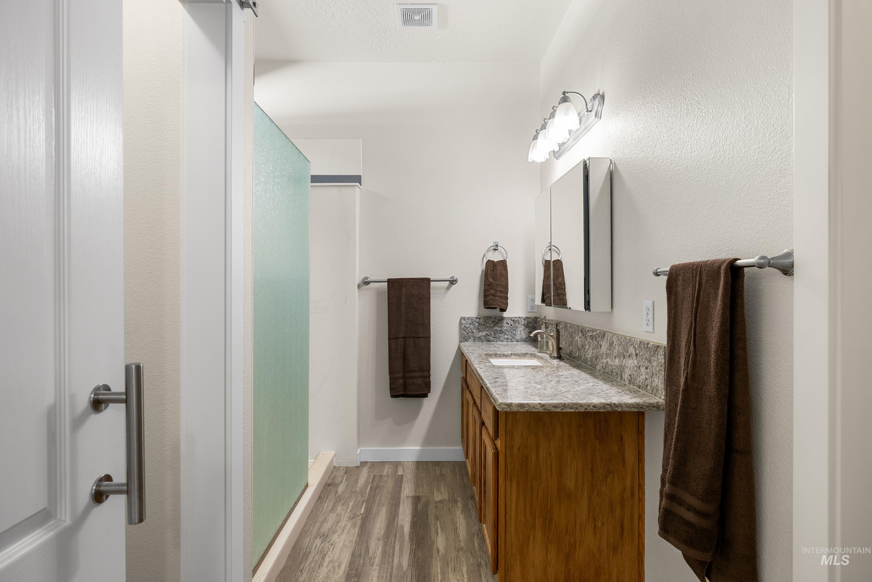 Full bath featuring light wood-style flooring, a stall shower, and vanity