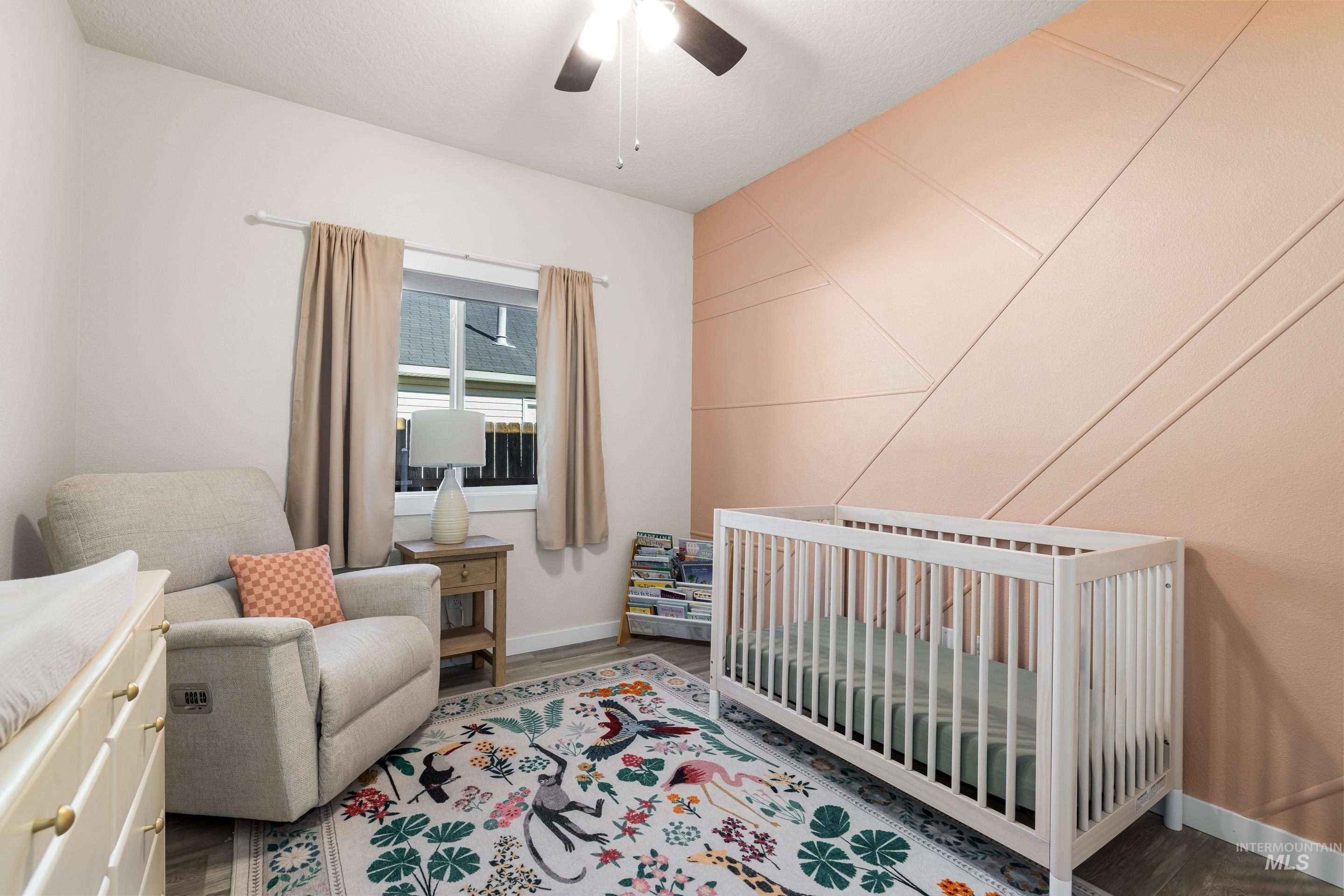 Bedroom featuring a crib, ceiling fan, and wood finished floors