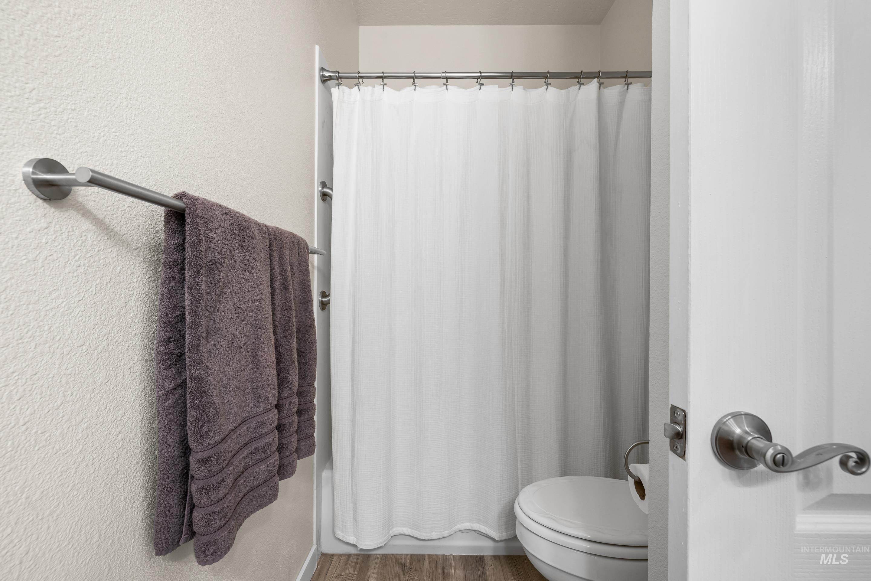Bathroom featuring a shower with shower curtain, wood finished floors, and a textured wall