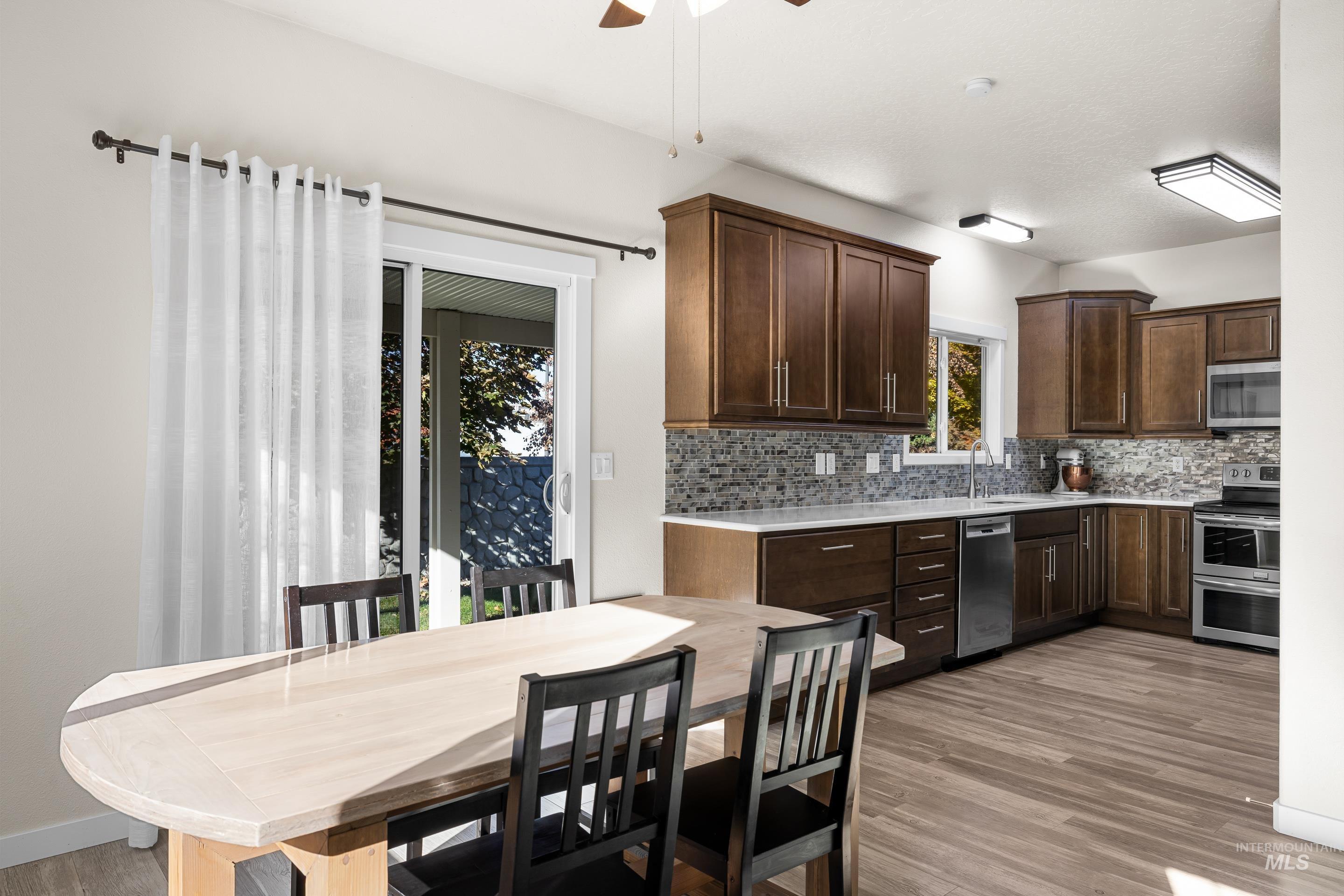 Kitchen featuring dark brown cabinets, decorative backsplash, light wood finished floors, and appliances with stainless steel finishes