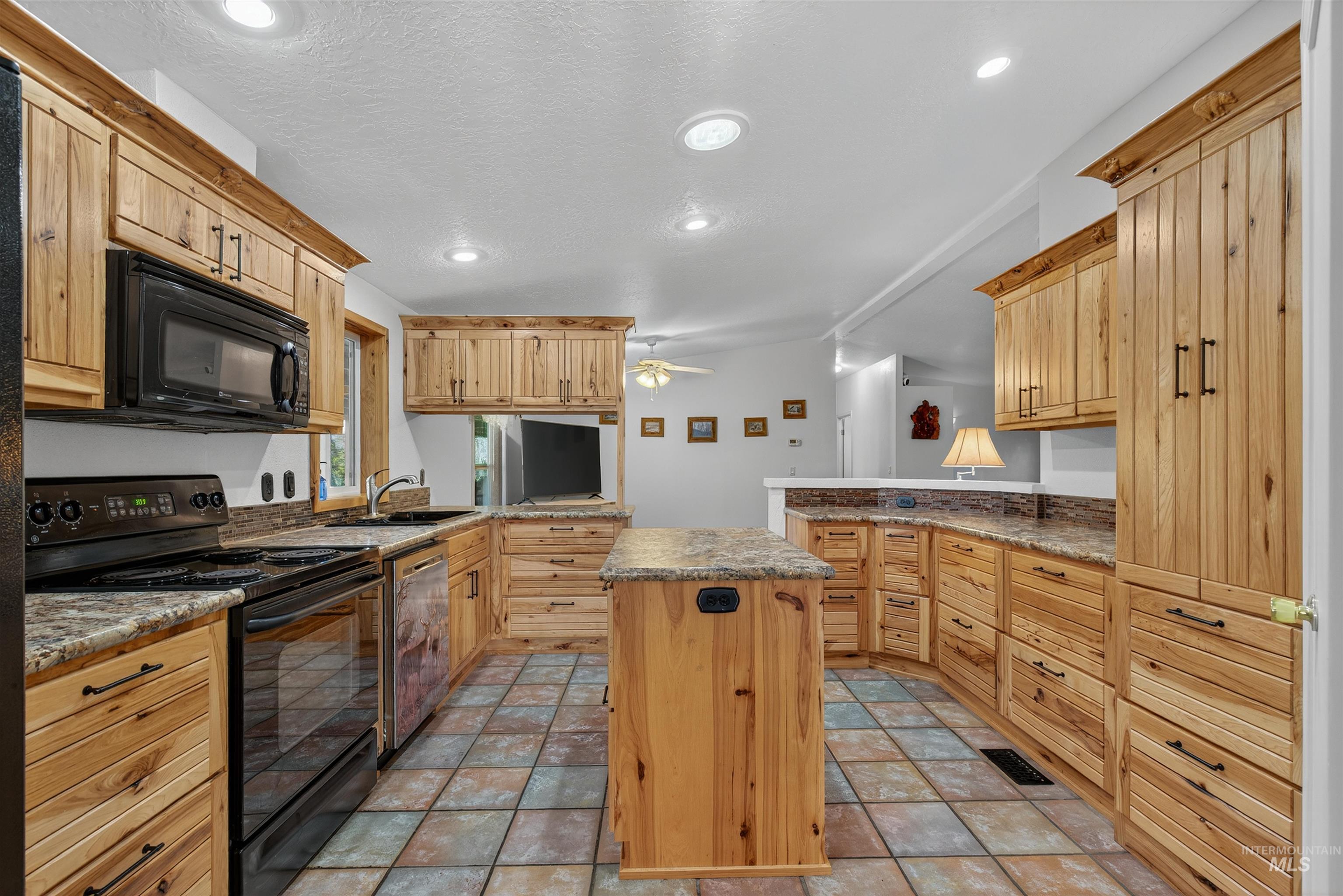 Kitchen with a peninsula, black appliances, a kitchen island, a ceiling fan, and vaulted ceiling