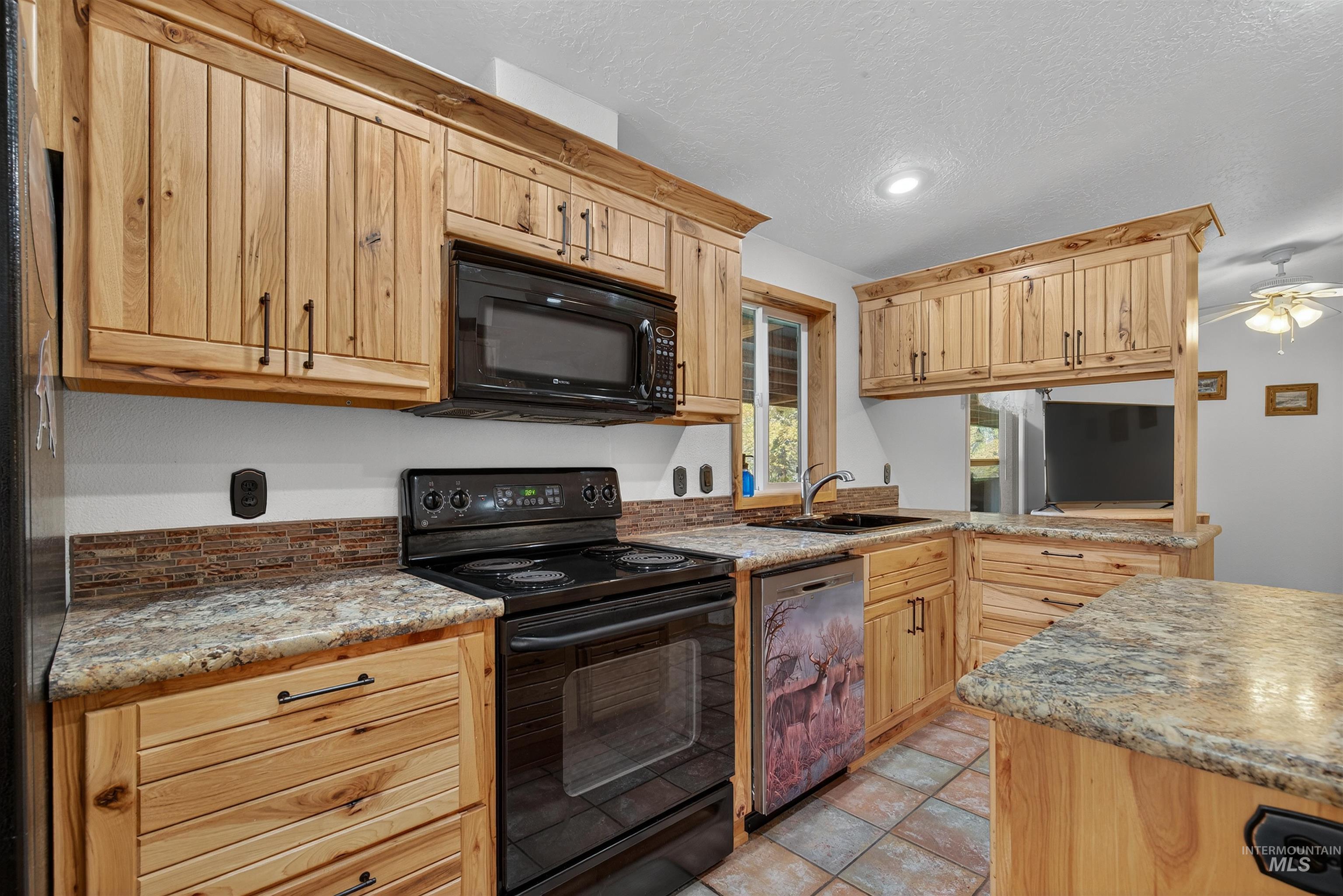Kitchen featuring black appliances, a textured ceiling, light stone counters, a peninsula, and light brown cabinets