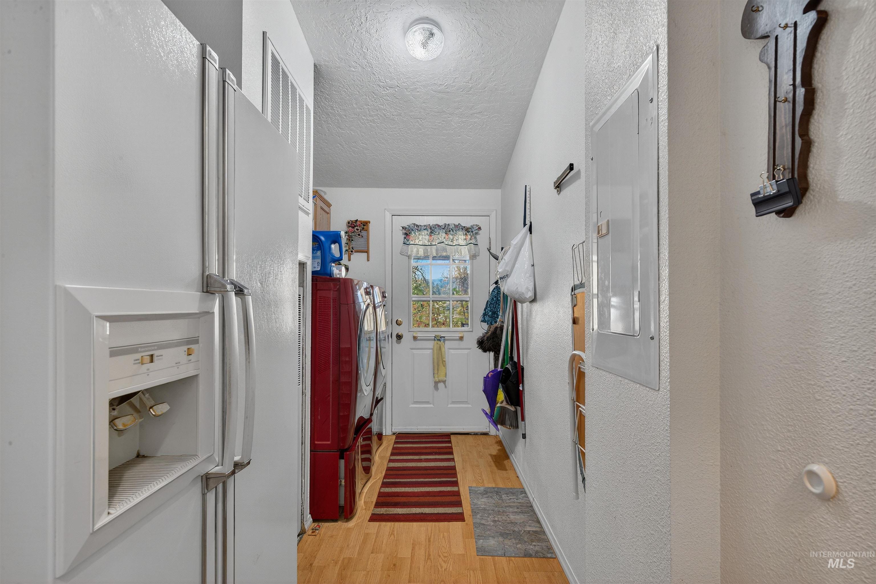 Doorway with wood finished floors, electric panel, a textured ceiling, and a textured wall