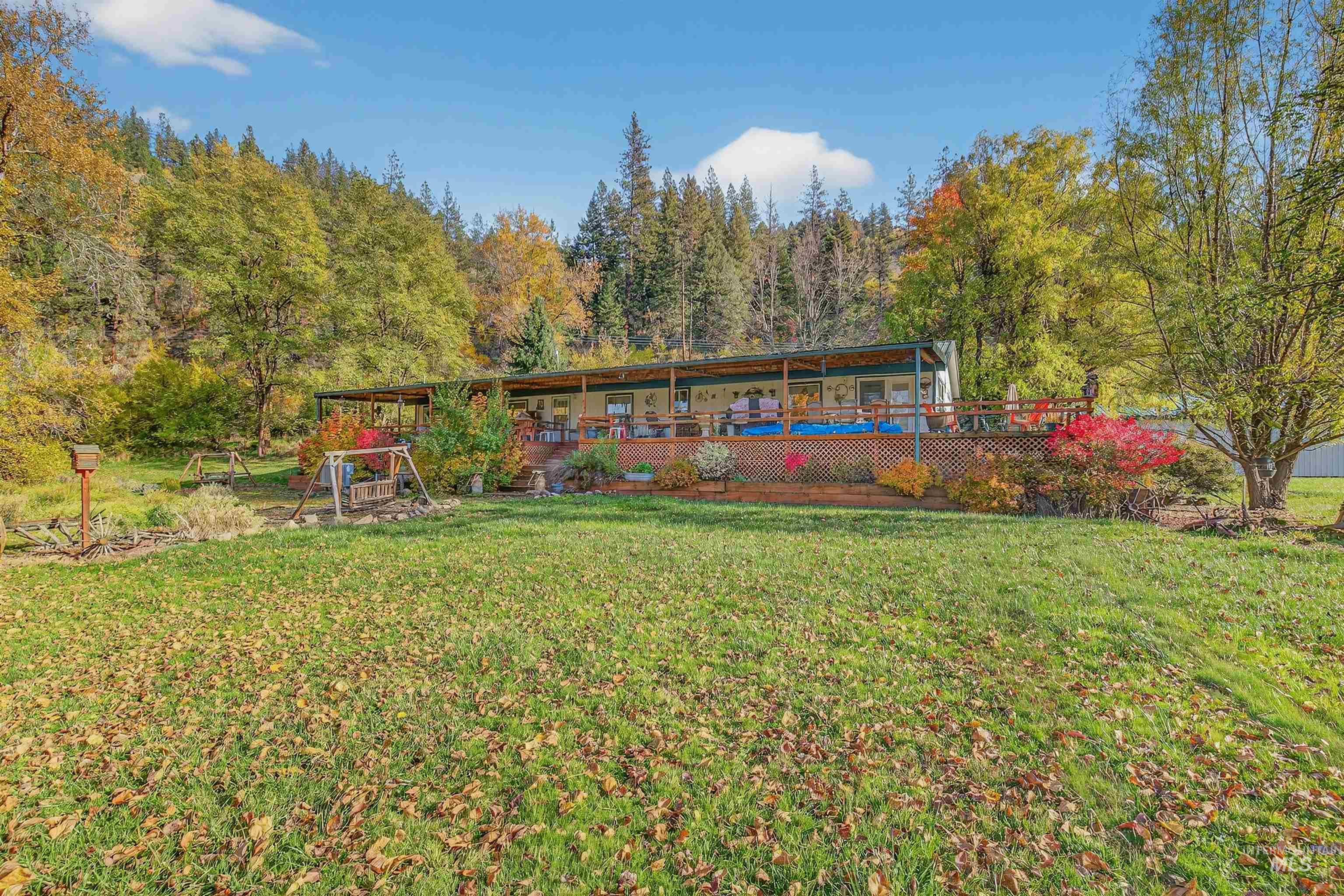 Back of property with a wooden deck, a lawn, and a wooded view