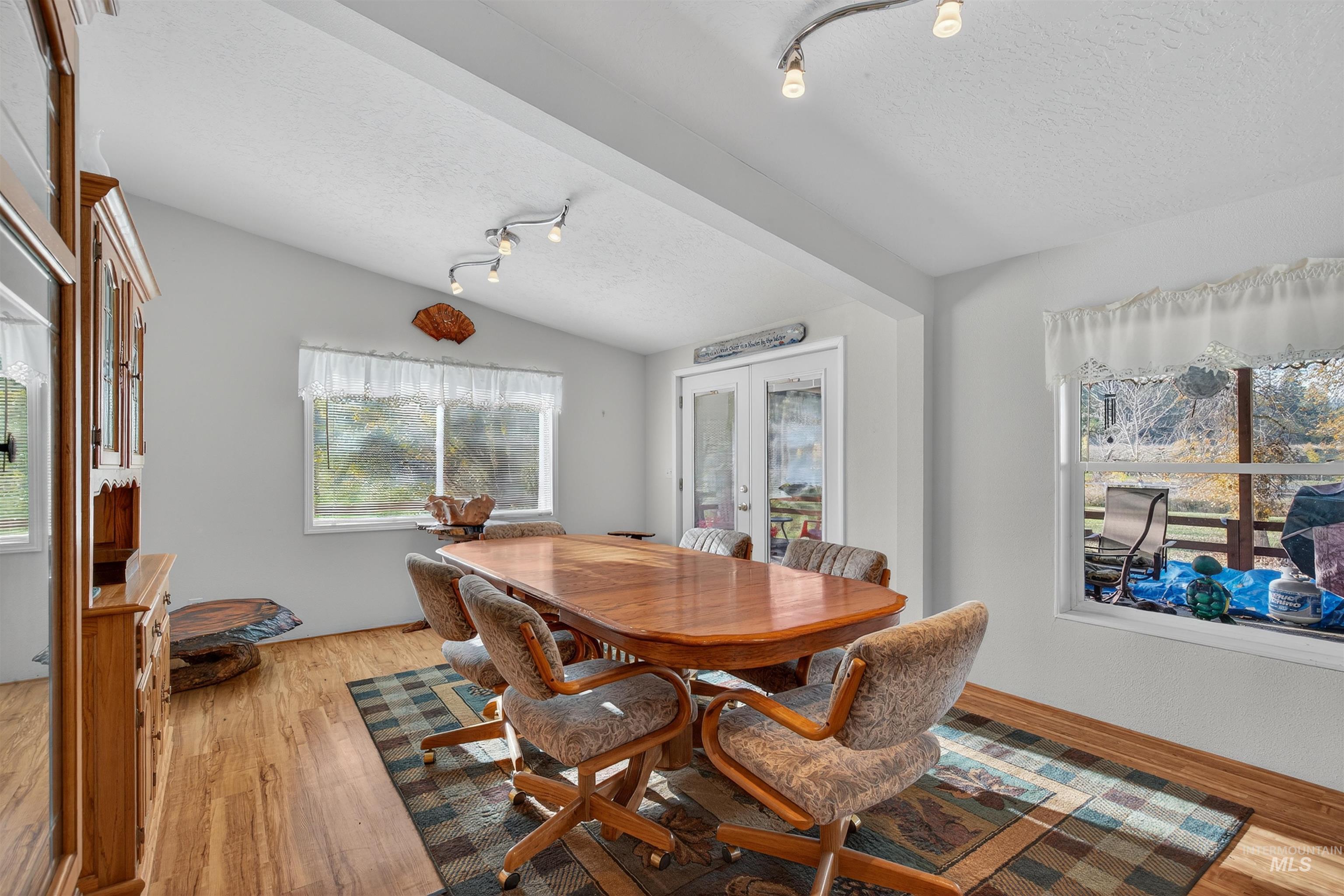 Dining area featuring french doors, a textured ceiling, lofted ceiling, rail lighting, and light wood-style flooring