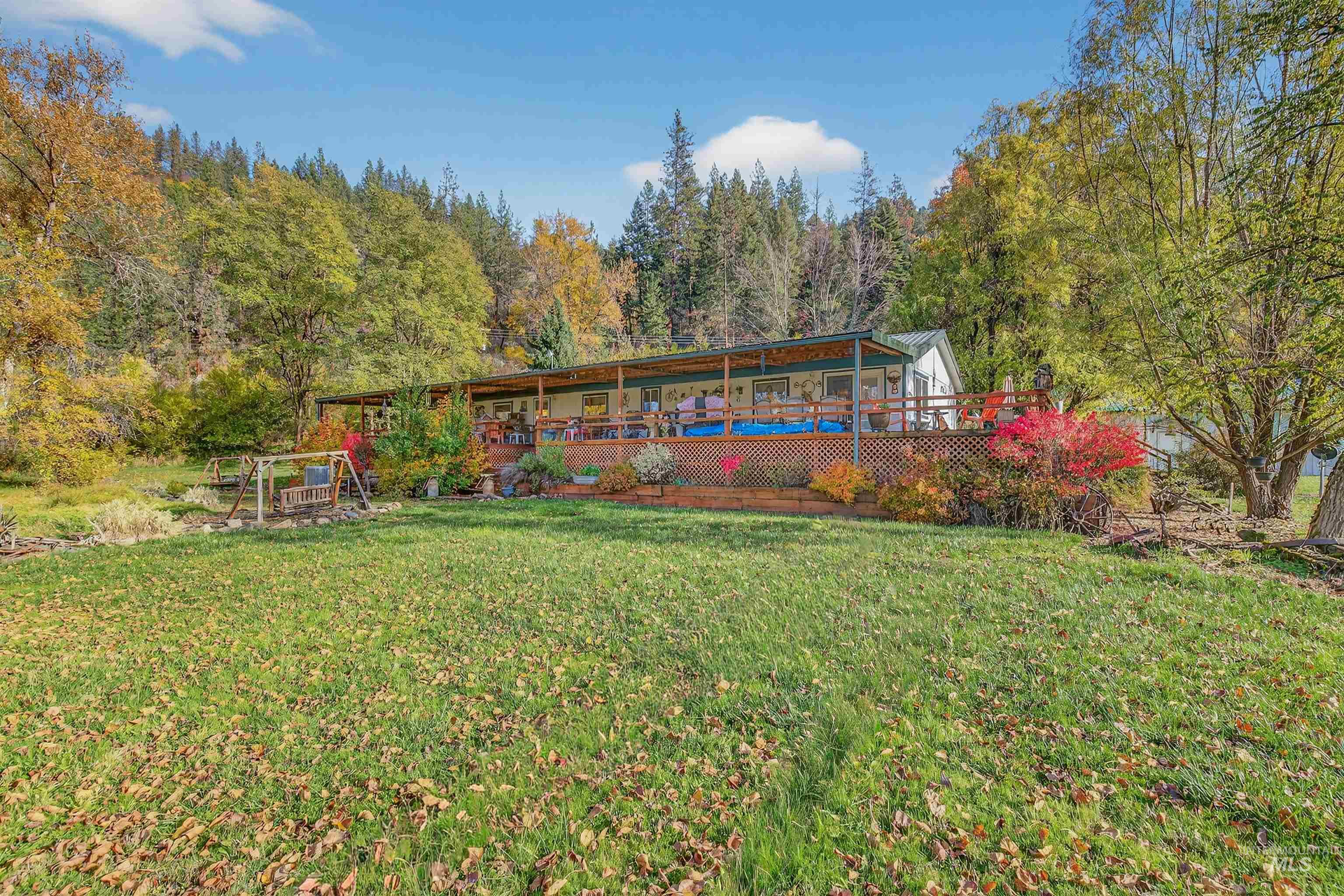 Rear view of house with a deck, a lawn, and a forest view