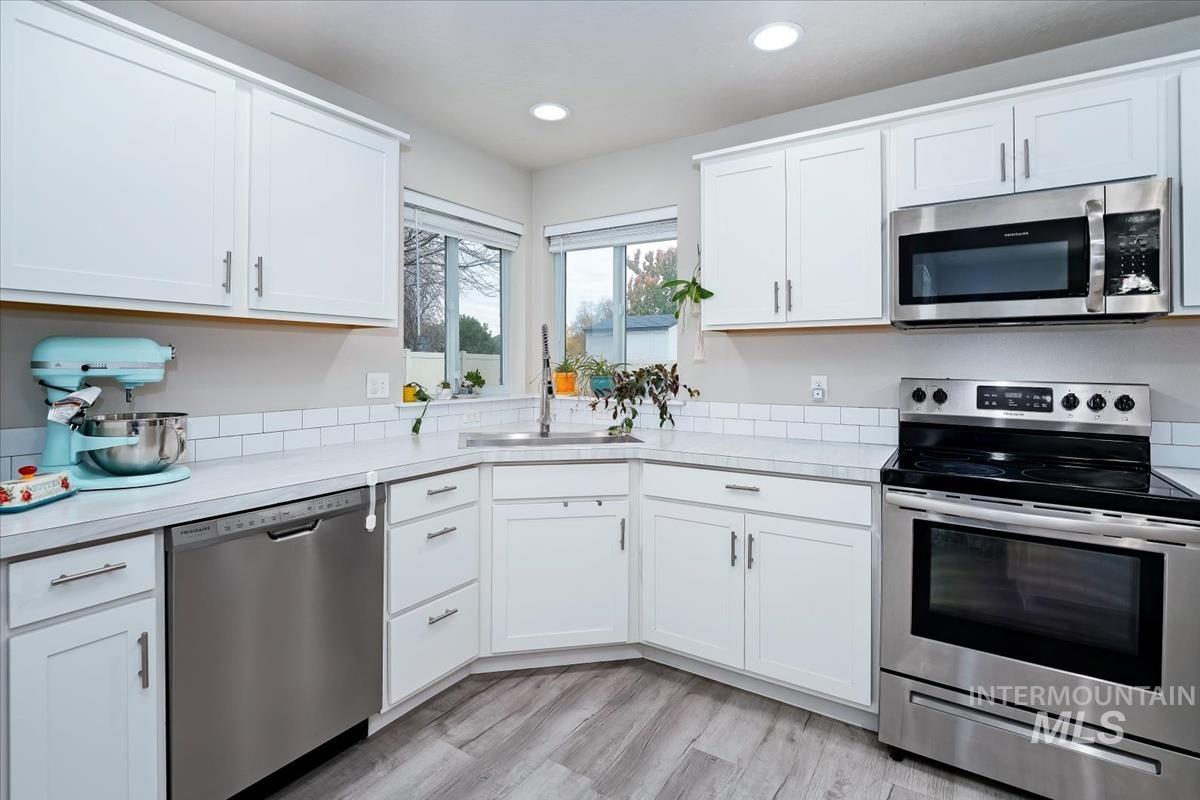 Kitchen with stainless steel appliances, light countertops, white cabinetry, recessed lighting, and light wood-style floors