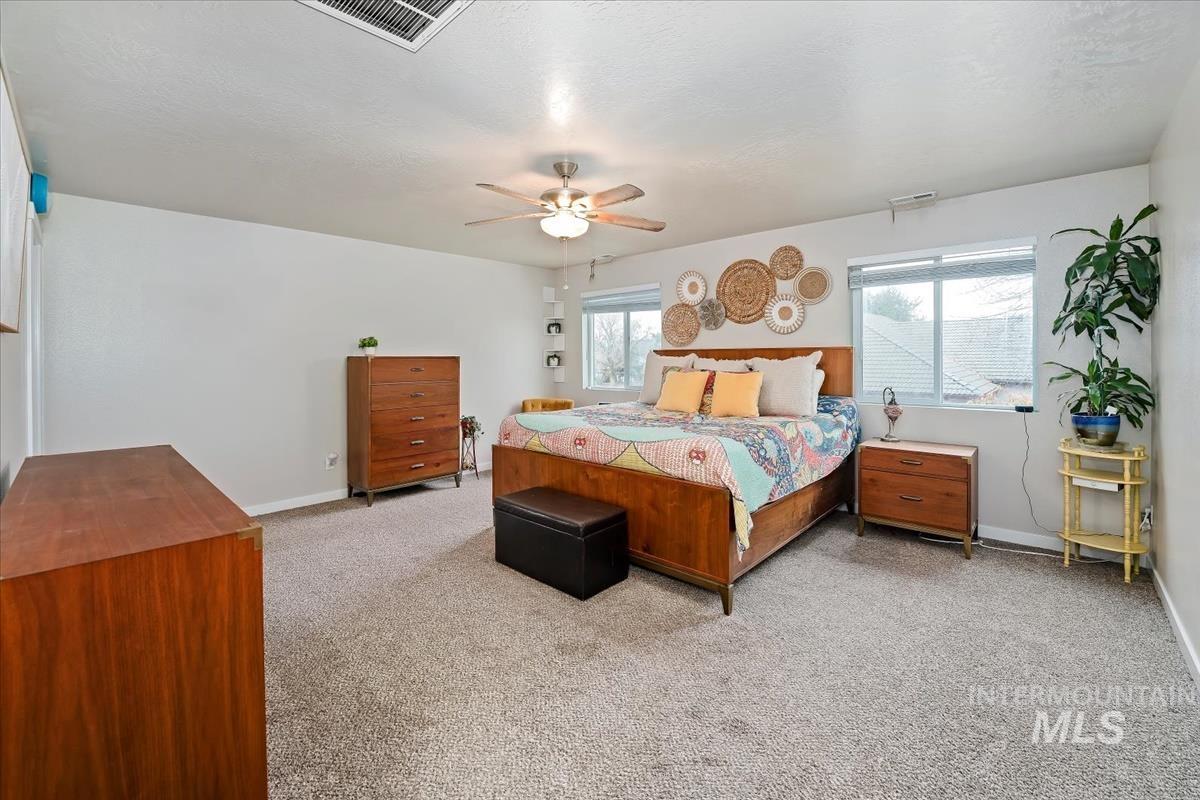 Bedroom featuring light colored carpet, multiple windows, and ceiling fan