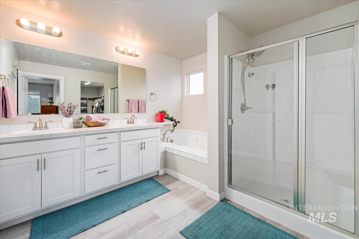 Full bath with double vanity, a walk in closet, light wood-type flooring, a garden tub, and a shower stall