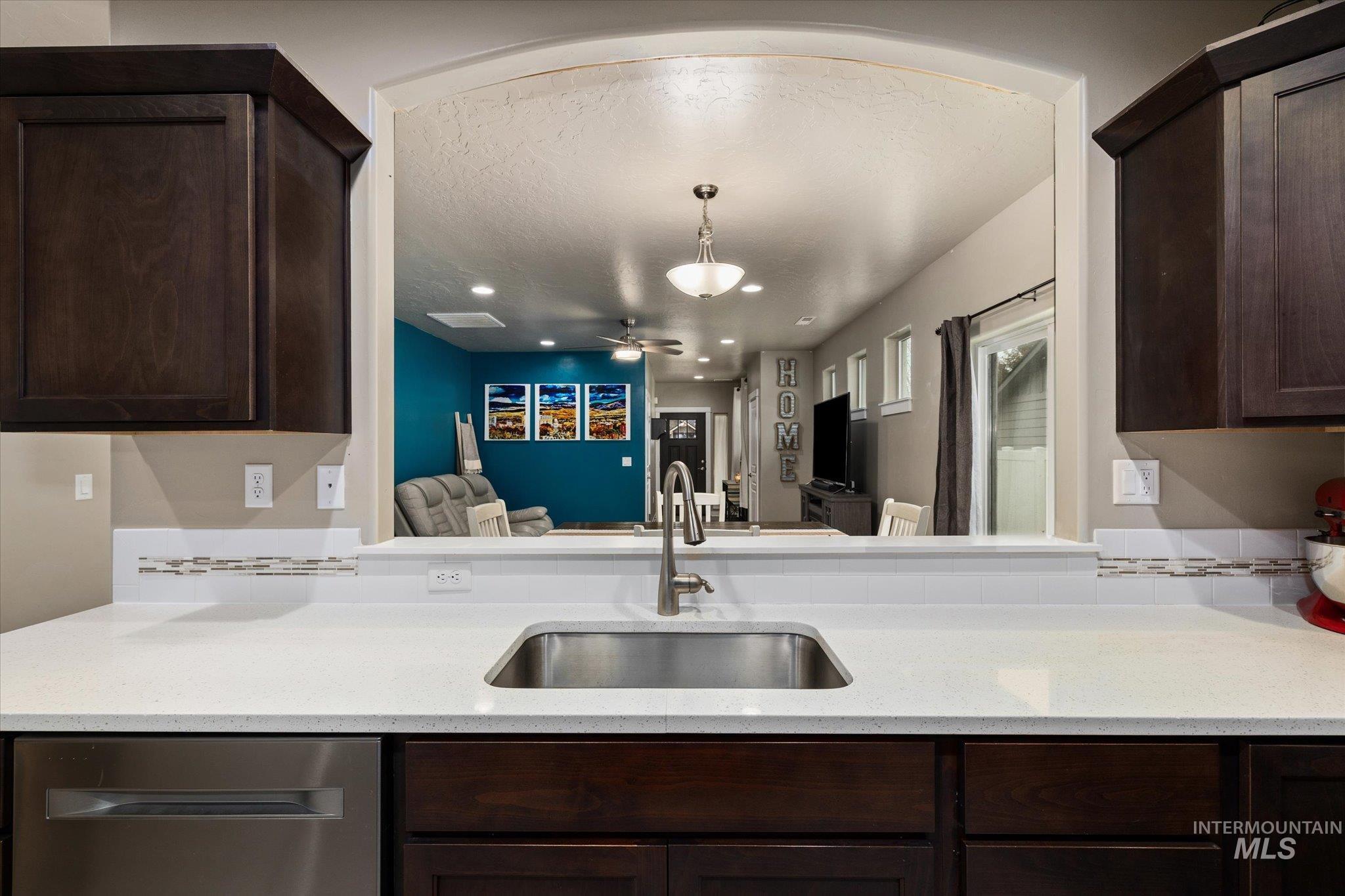 Kitchen featuring dark brown cabinetry, dishwasher, light stone counters, hanging light fixtures, and ceiling fan