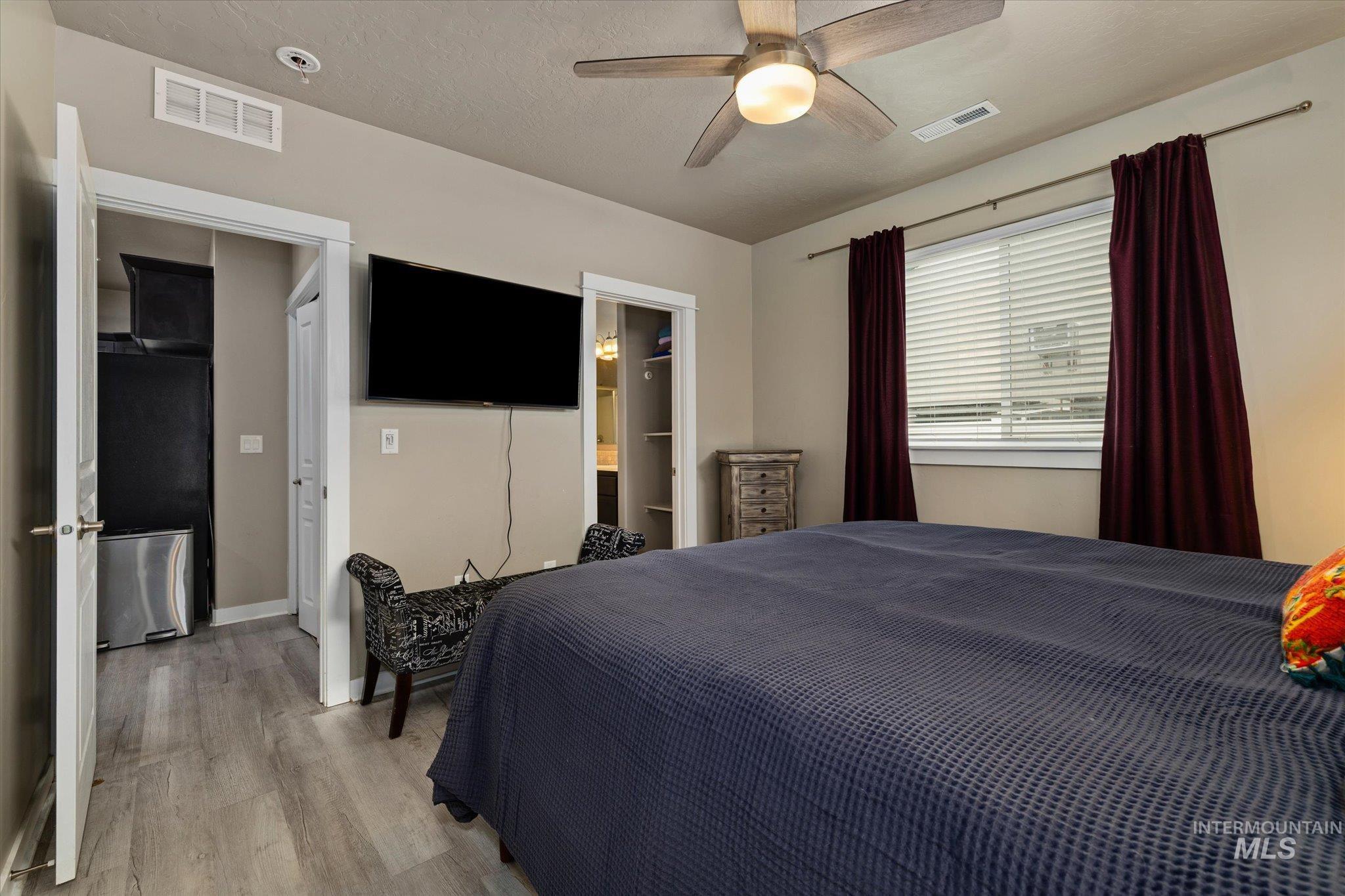 Bedroom featuring wood finished floors, ceiling fan, ensuite bath, and freestanding refrigerator