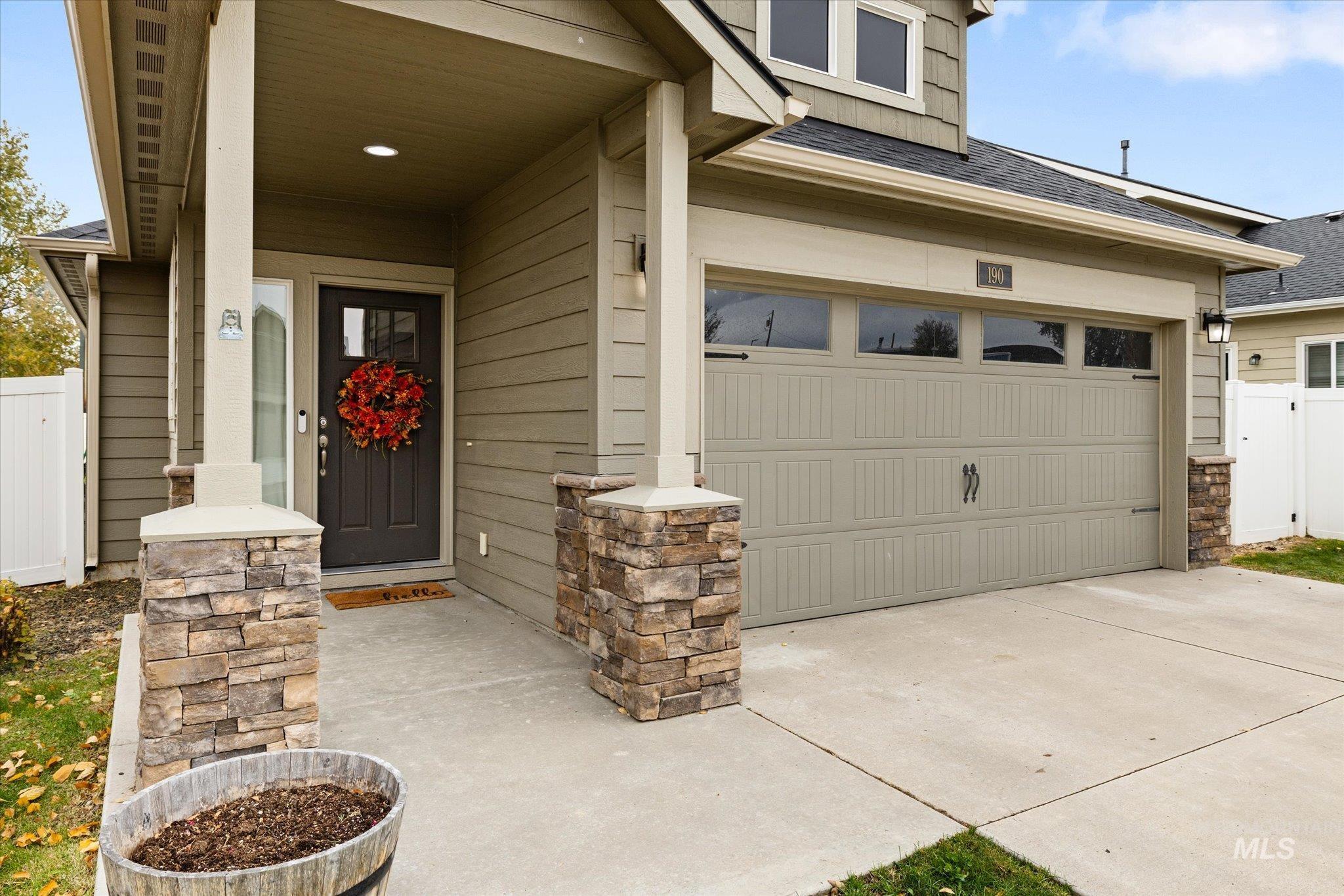 Entrance to property with a shingled roof, a garage, concrete driveway, and a porch