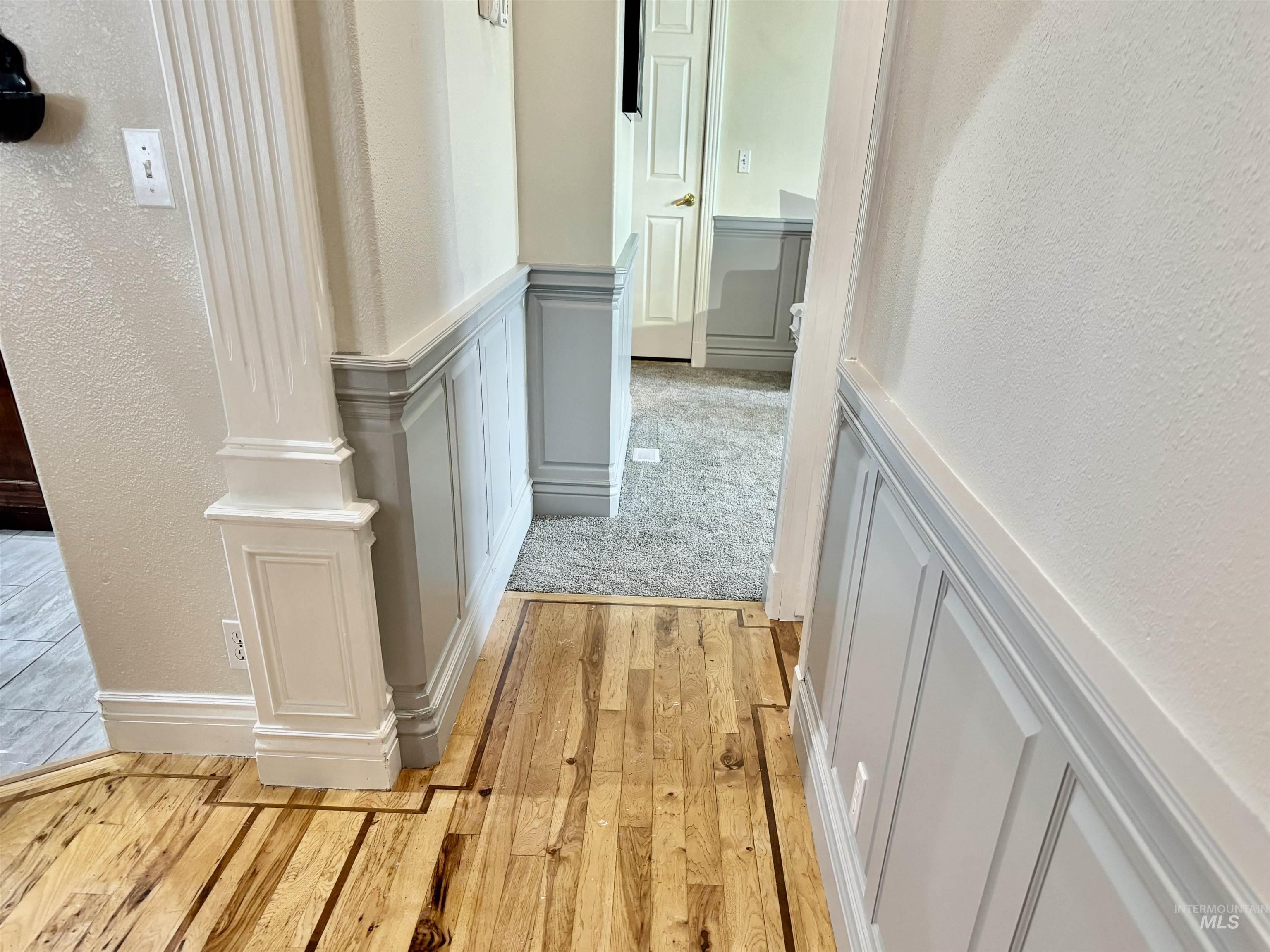 Hall featuring a decorative wall, light wood-style flooring, wainscoting, and a textured wall