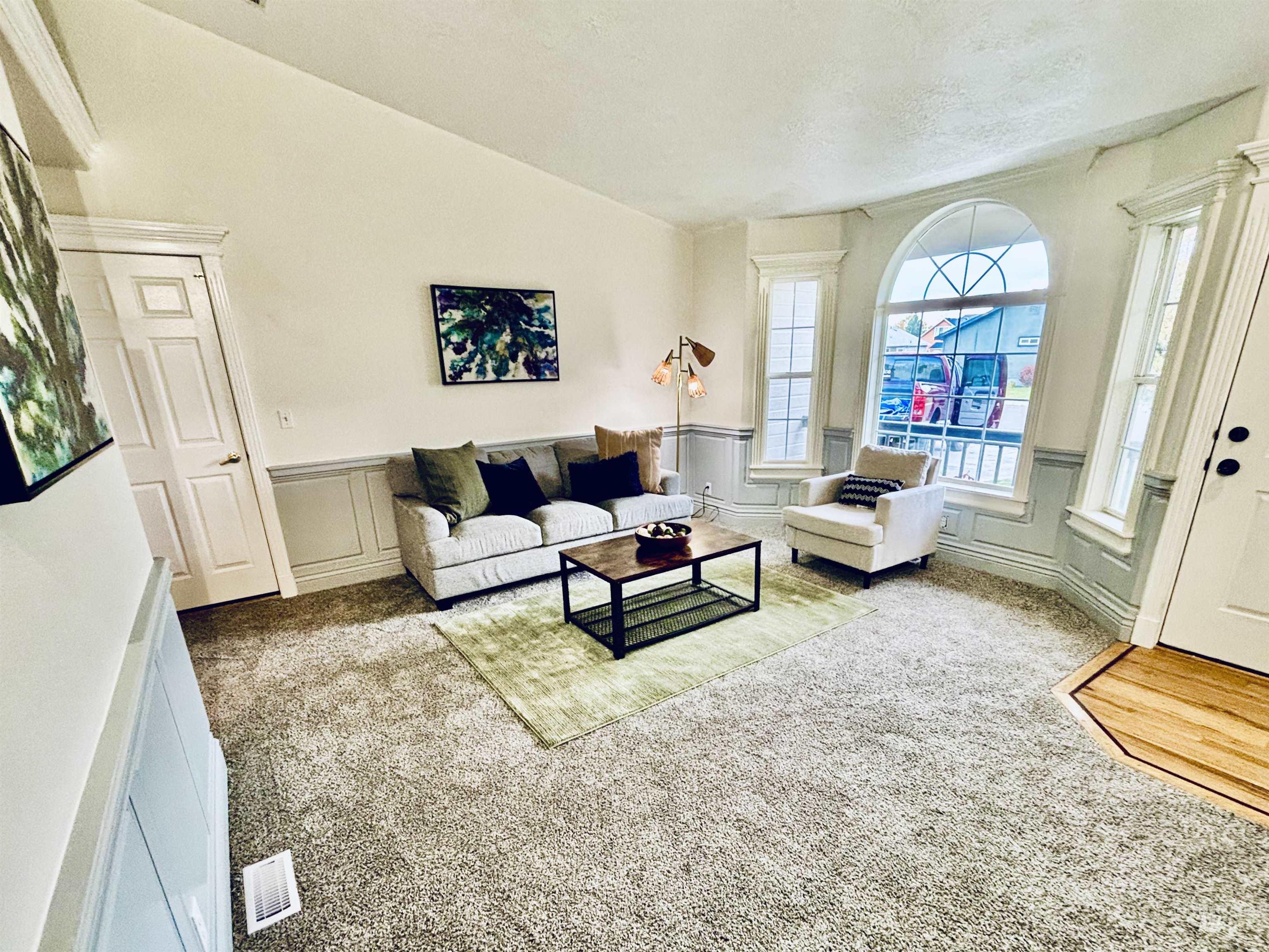 Living room featuring carpet flooring, a decorative wall, lofted ceiling, and a wainscoted wall
