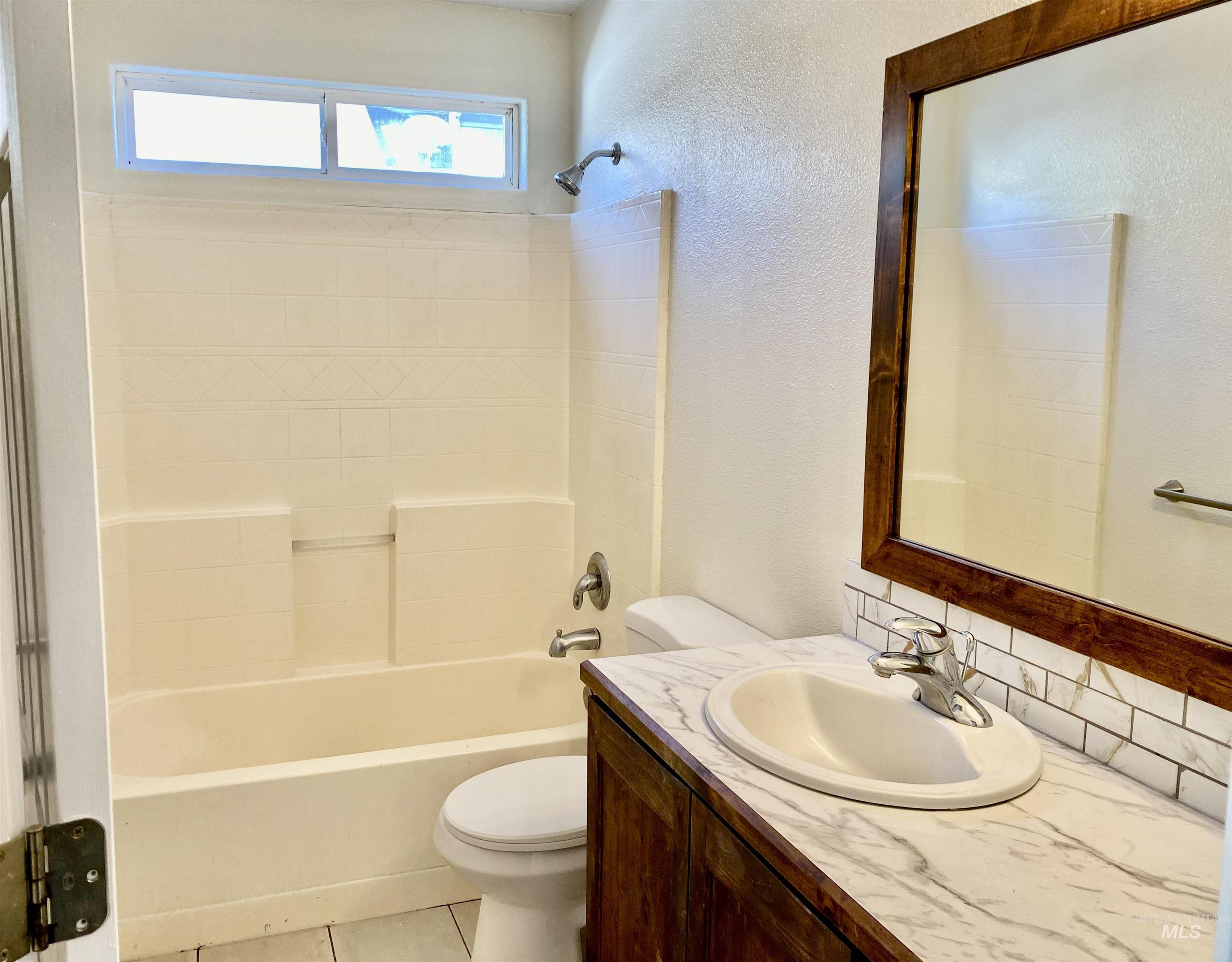 Full bath featuring vanity, a textured wall, light tile patterned floors, shower / tub combination, and decorative backsplash