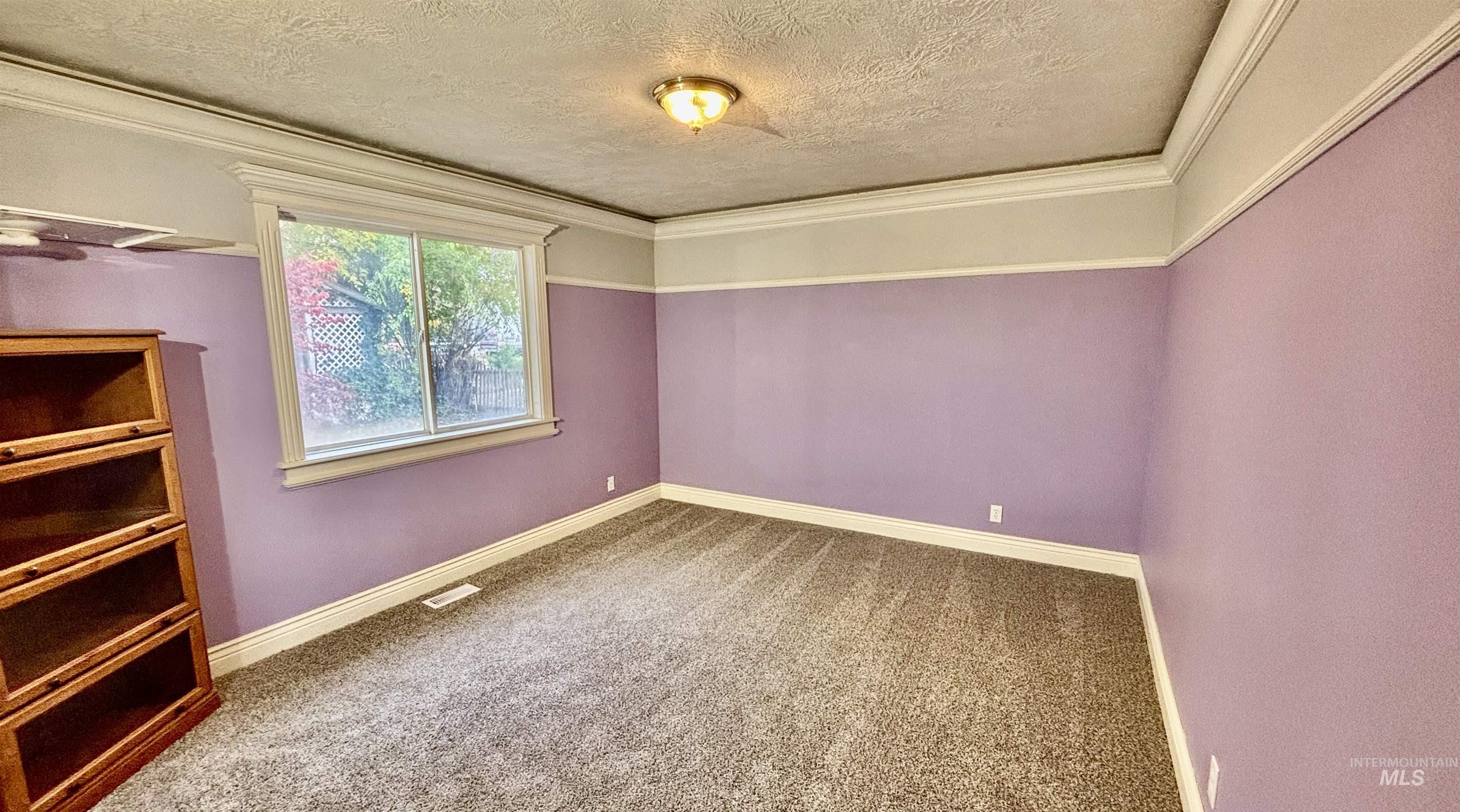 Empty room featuring carpet, a textured ceiling, and ornamental molding