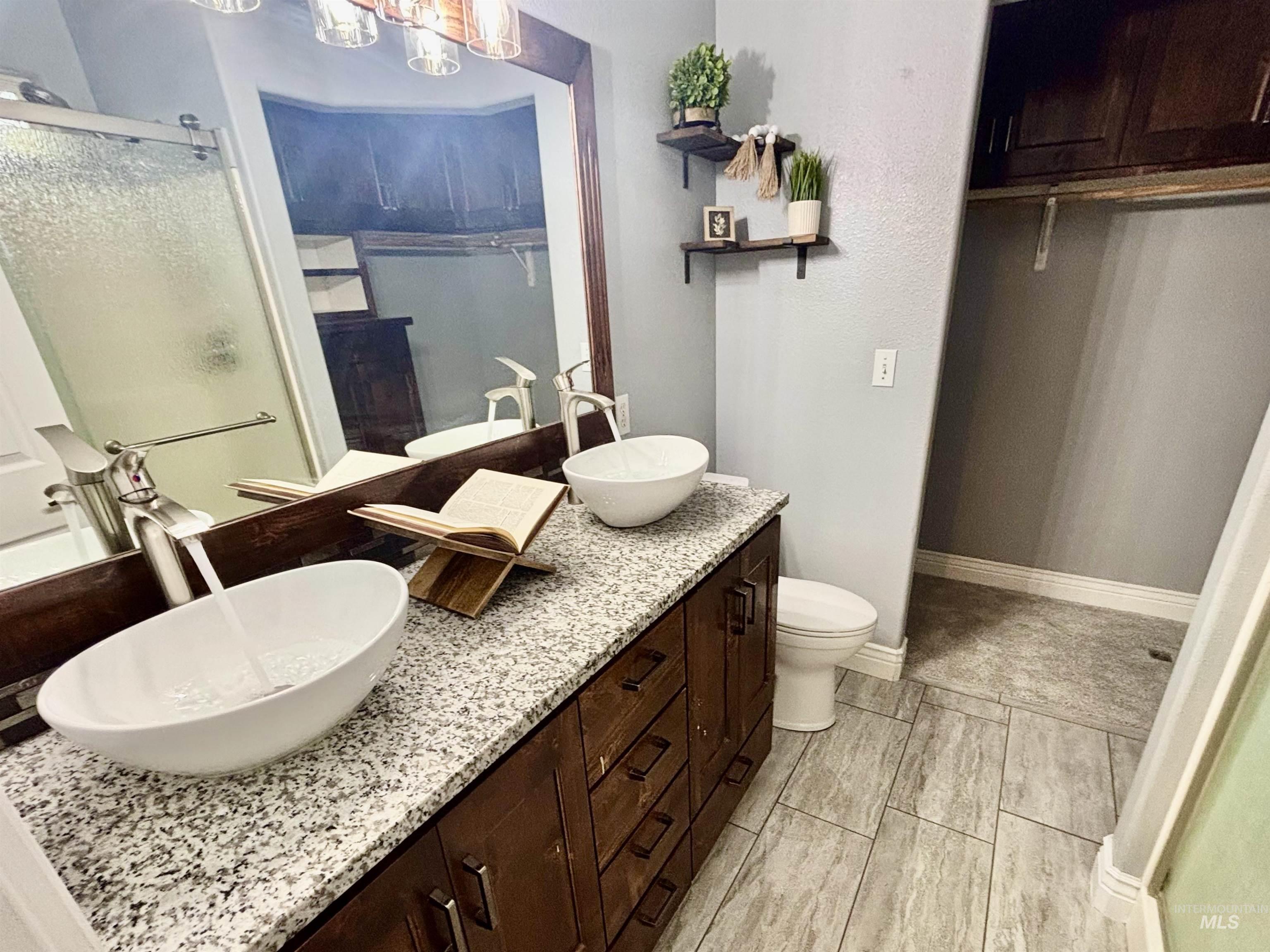 Bathroom featuring a stall shower, double vanity, a walk in closet, and wood finish floors