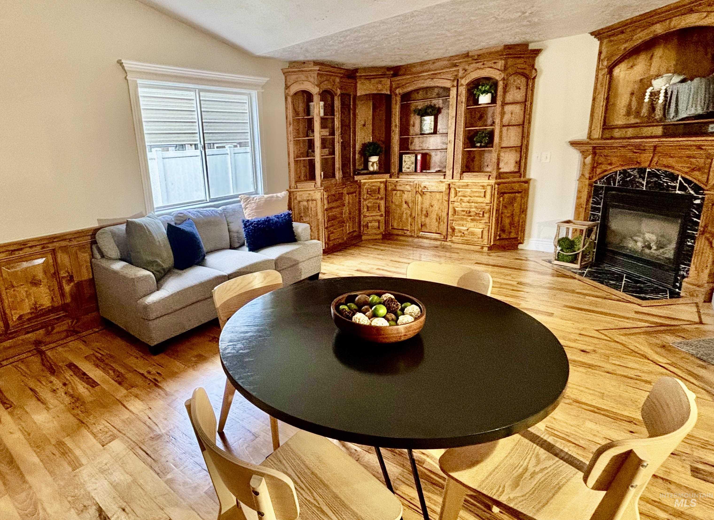 Living room with a textured ceiling, a high end fireplace, light wood-type flooring, and vaulted ceiling