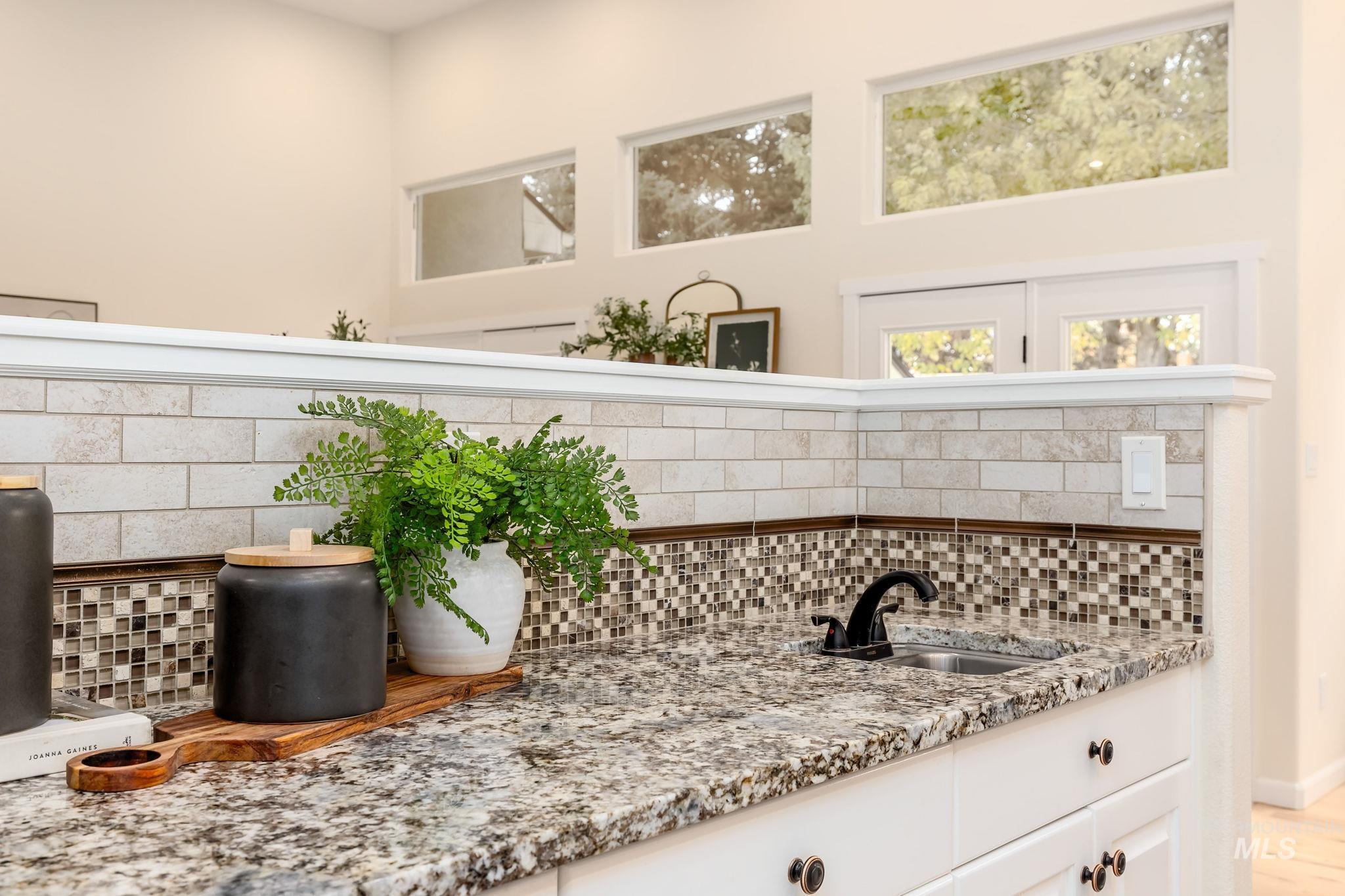 Detailed view of decorative backsplash, light stone countertops, white cabinets, and open shelves