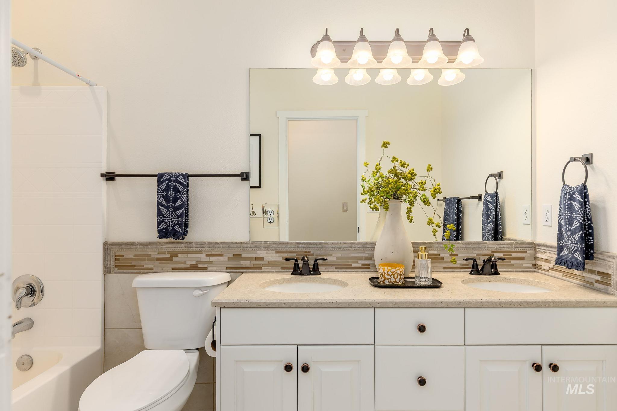 Bathroom with double vanity, shower / washtub combination, and backsplash