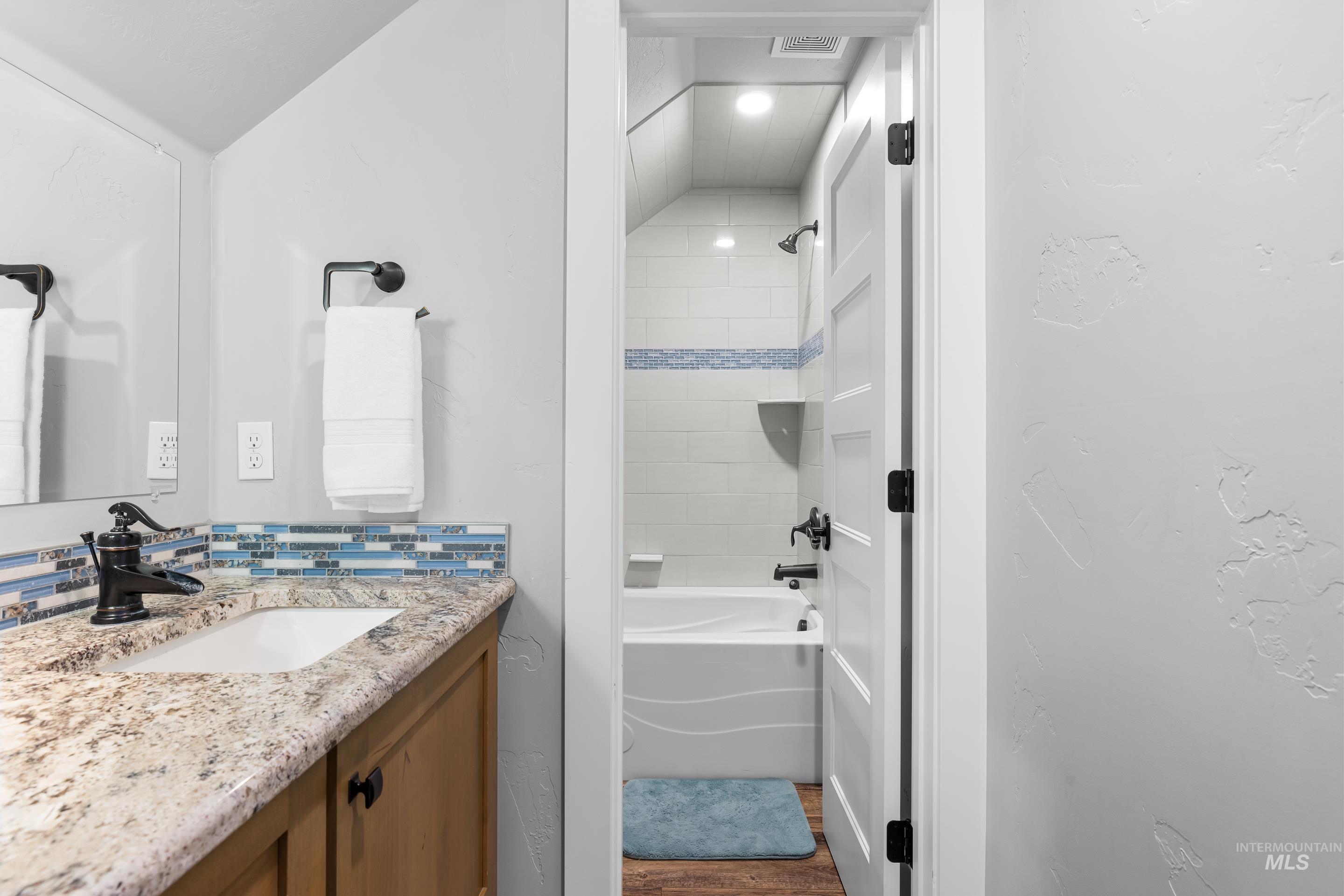 Bathroom with  shower combination, vanity, dark wood-type flooring, and vaulted ceiling