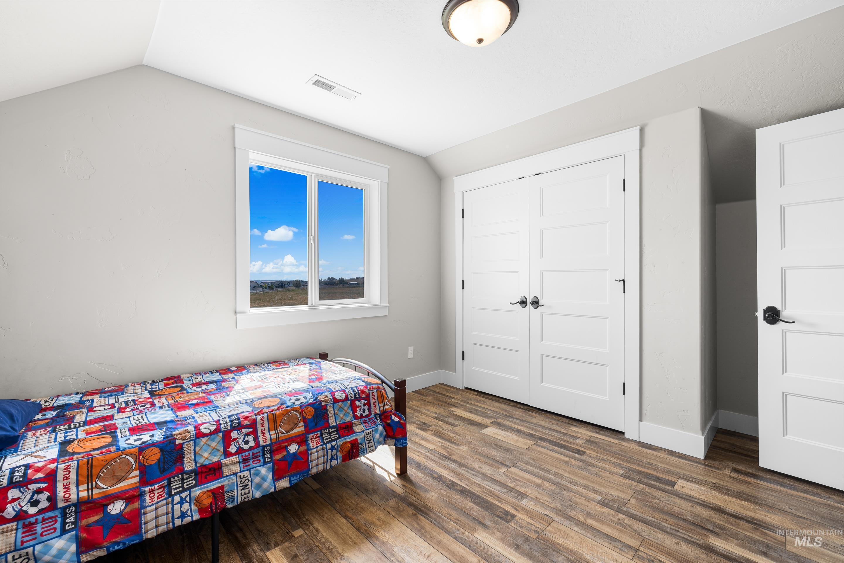 Bedroom featuring dark wood-style flooring, vaulted ceiling, and a closet