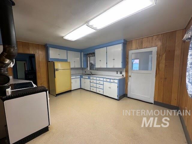 Kitchen with wooden walls, white cabinetry, freestanding refrigerator, light countertops, and light flooring