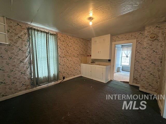 Spare room featuring wallpapered walls, a textured ceiling, and dark colored carpet